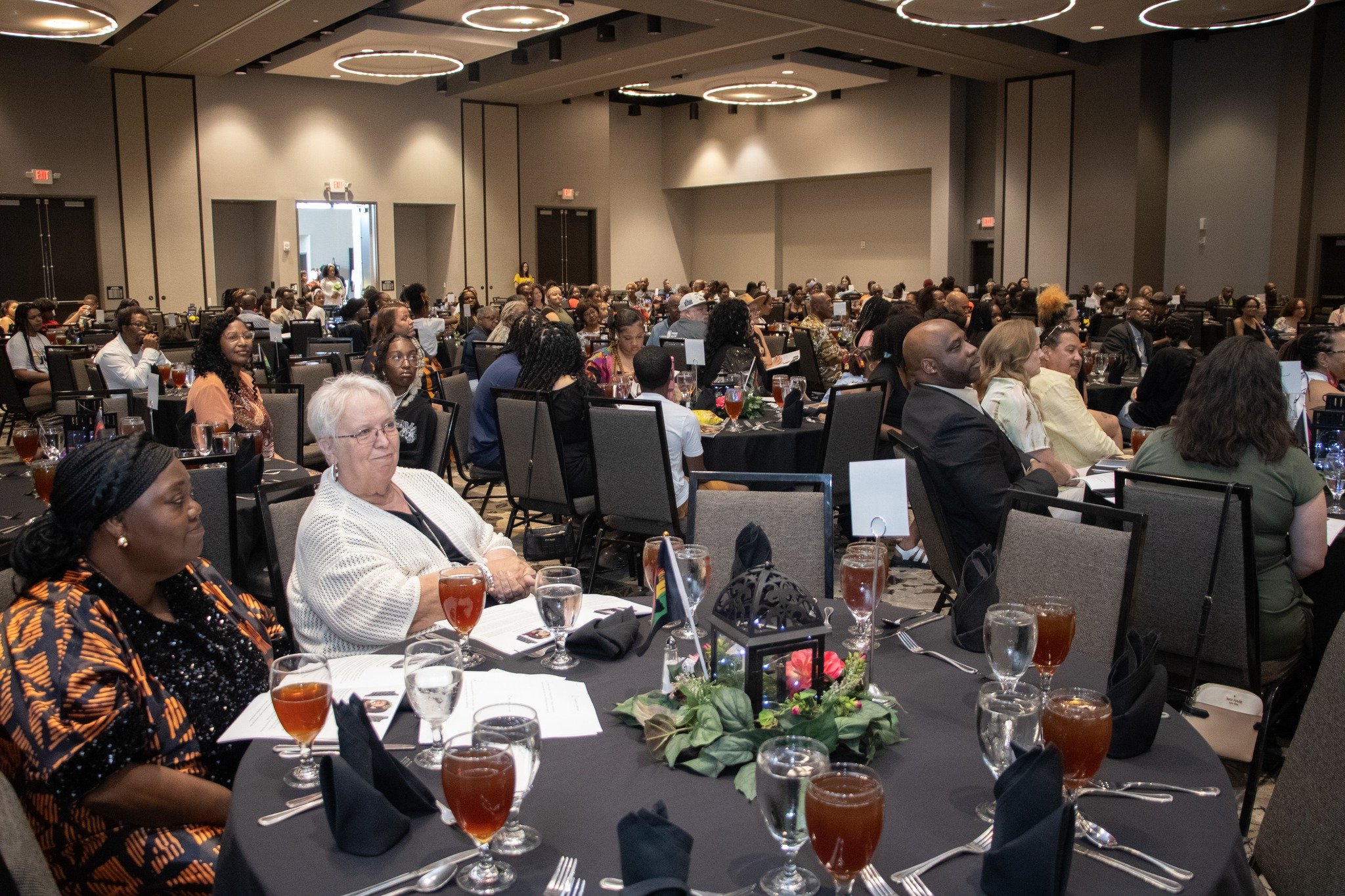 Crowd of people seated at round tables in a large banquet hall, attending a formal event or conference.