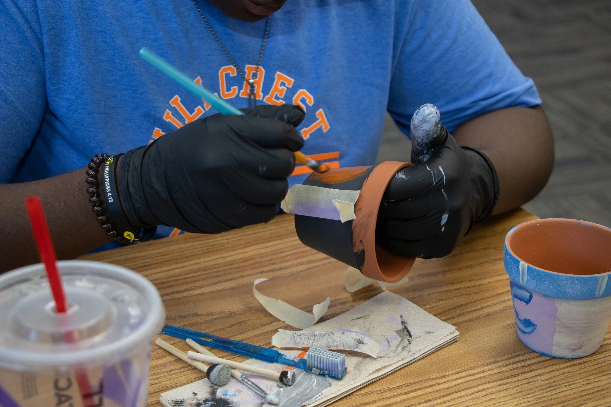 Person painting a ceramic or clay pot at a table with painting supplies, including brushes and paper towels.