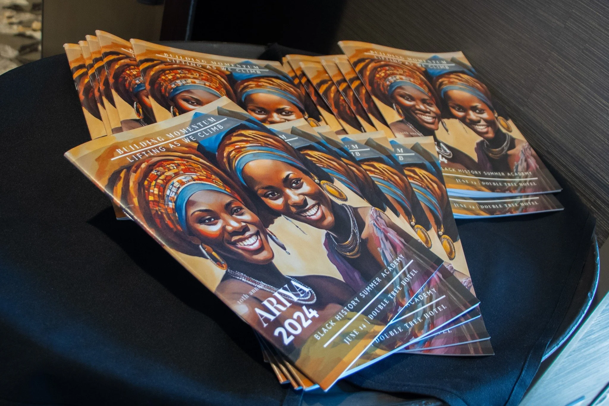 Flyer or brochure with a smiling woman wearing traditional African attire and jewelry, text about building momentum and lifting as we climb, date July 24, 2022, promoting a black history summer academy at a hotel.