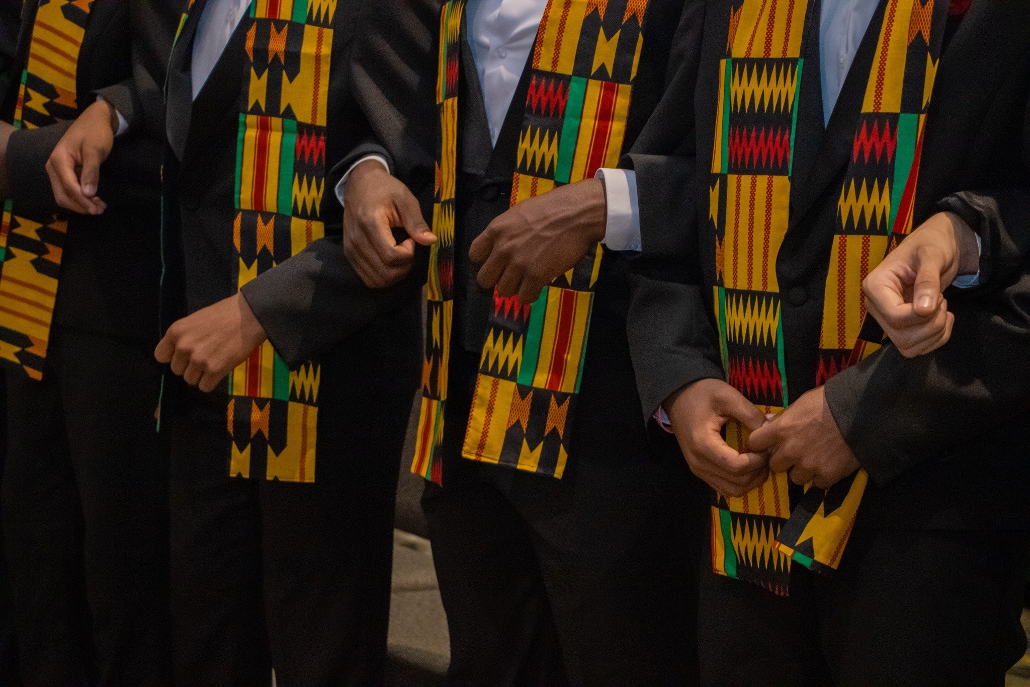 Group of people wearing black robes with colorful kente cloth stoles at a formal event.