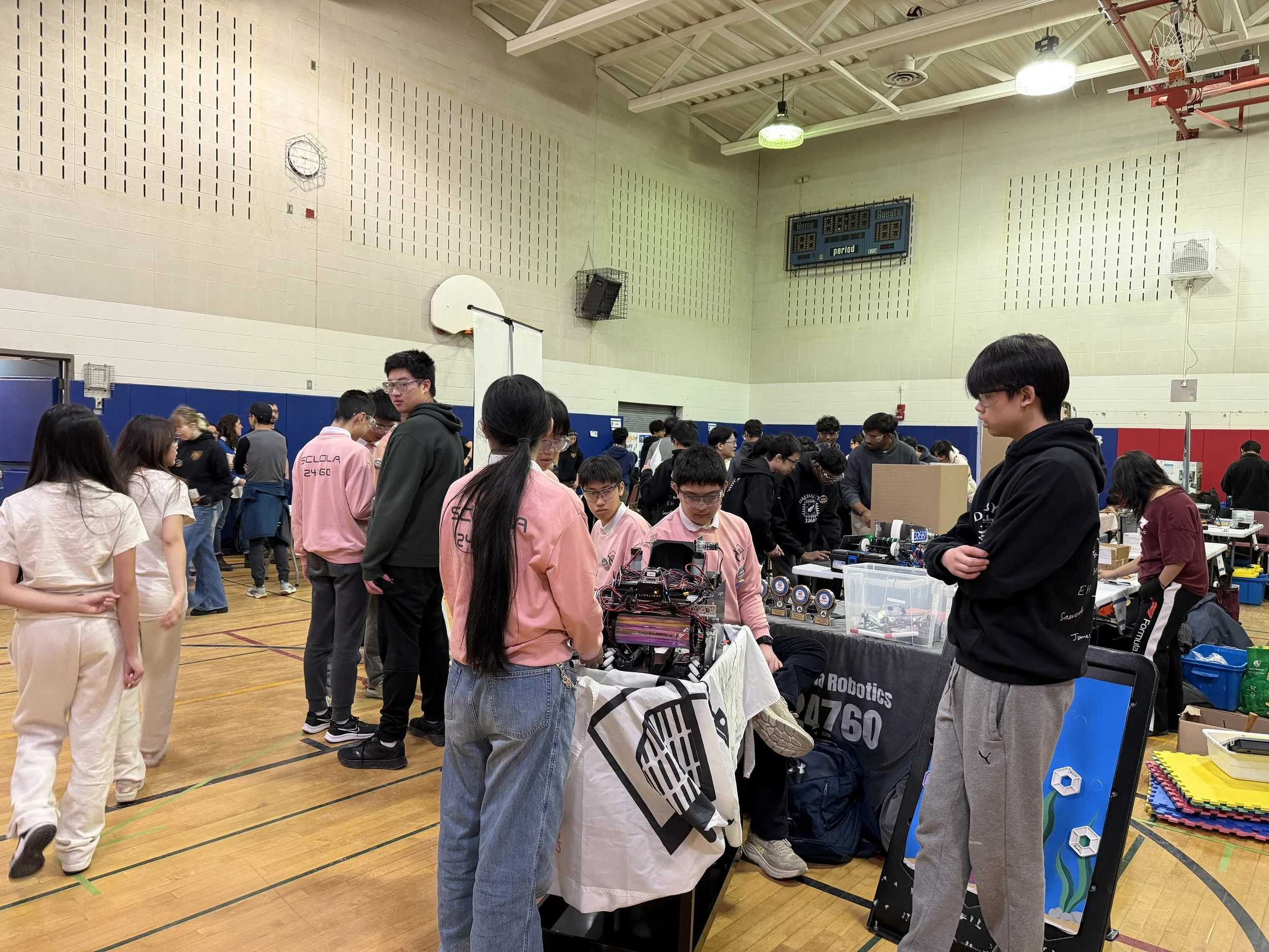 A group of students and people gathered in a gymnasium or large indoor space, showcasing various robotics projects and displays, with tables and equipment set up for a robotics event or competition.
