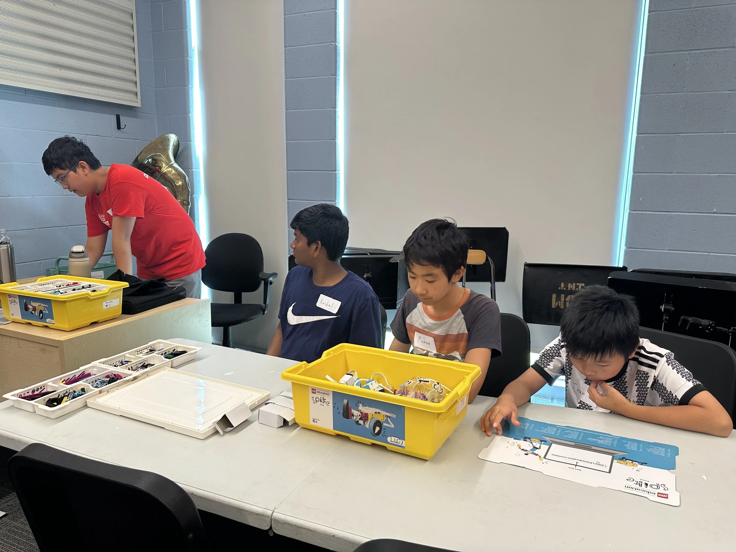 Four boys sitting at a table with LEGO robotics kits and an instructor preparing the building activity.