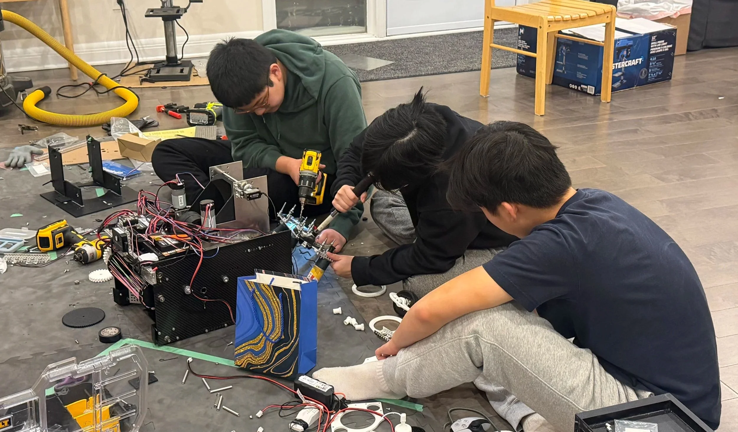 Three young people working together on assembling a robot with tools and electronic components on the floor.
