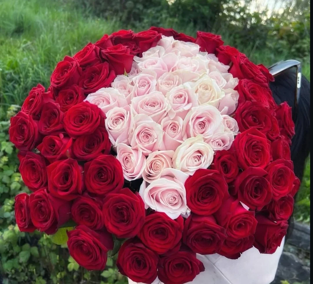 A bouquet of red, white, and pink roses arranged in a circular pattern outdoors.