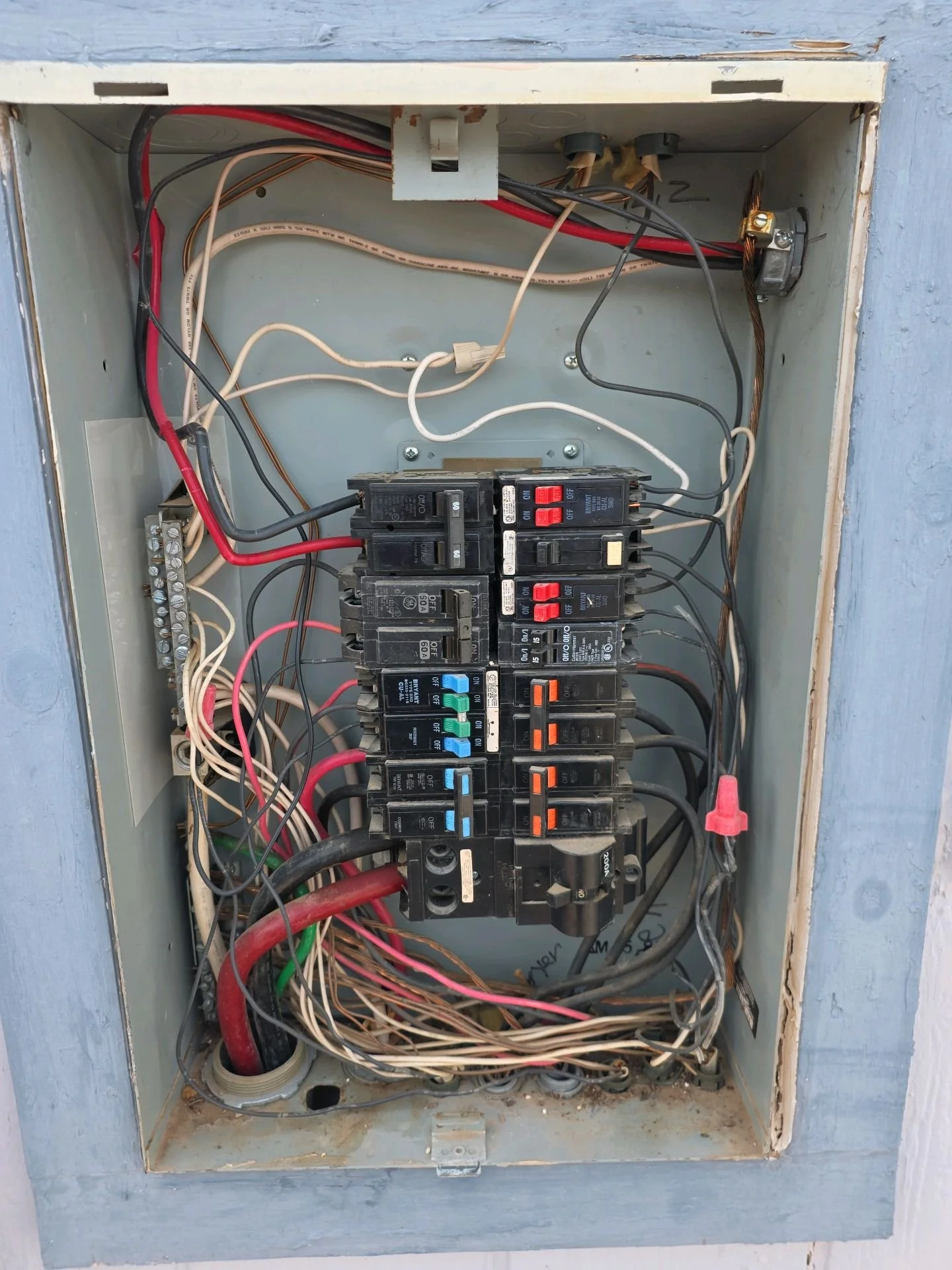 Electrical breaker box with various wires and circuit breakers inside, mounted in a gray metal box.