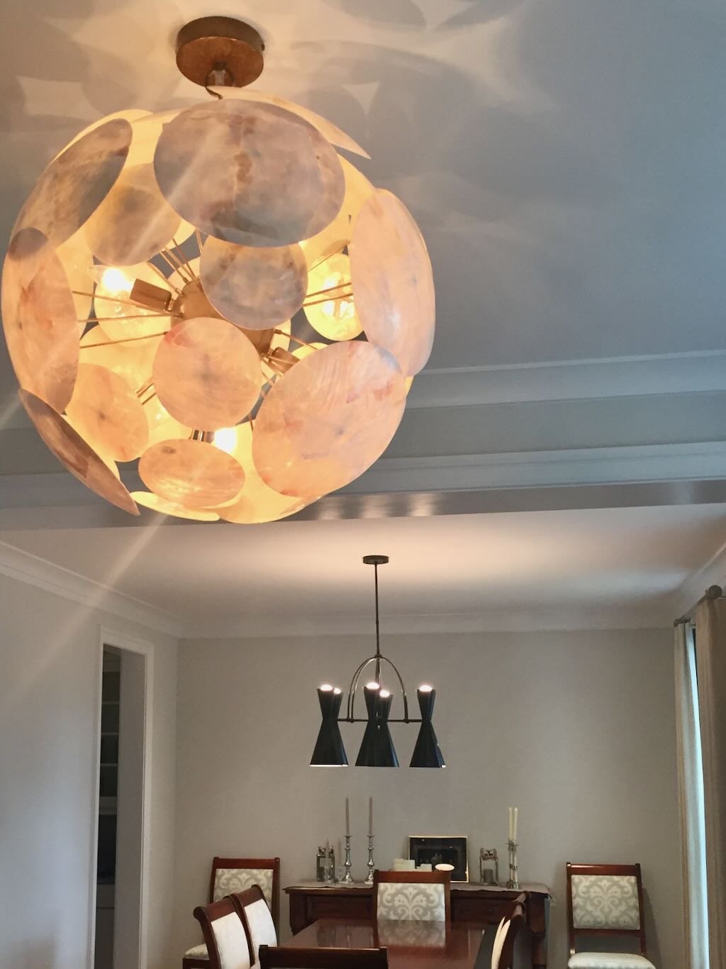 A living or dining room with a modern chandelier hanging over a dining table, and a decorative ceiling light fixture with shell-like circular piecesceiling light fixture with shell-like circular pieces