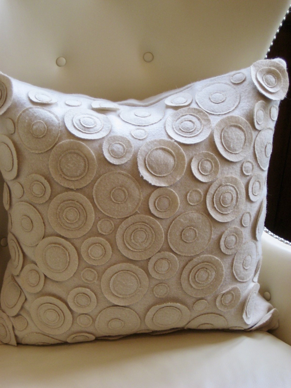 Decorative throw pillow with circular patterns on a beige armchair.