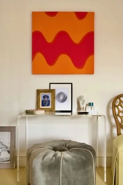 Decorative wall art and household decor on a white table, with a gray round ottoman in front.