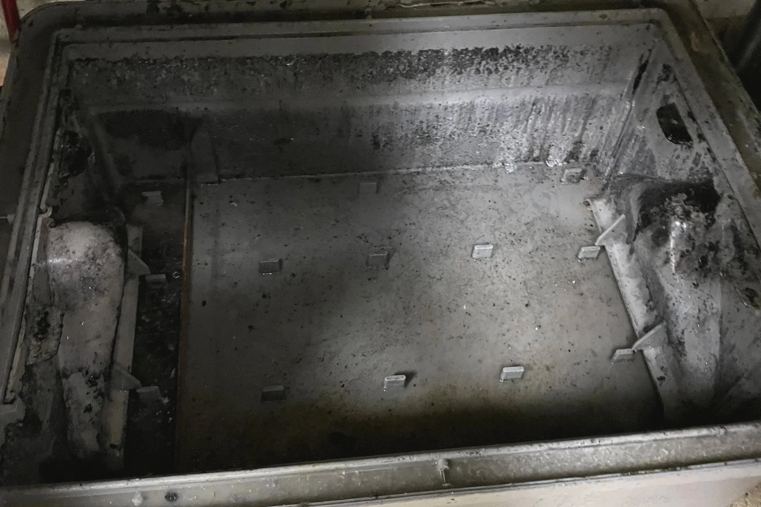 Inside of a burnt and charred metallic oven or microwave, with a soot-covered interior
