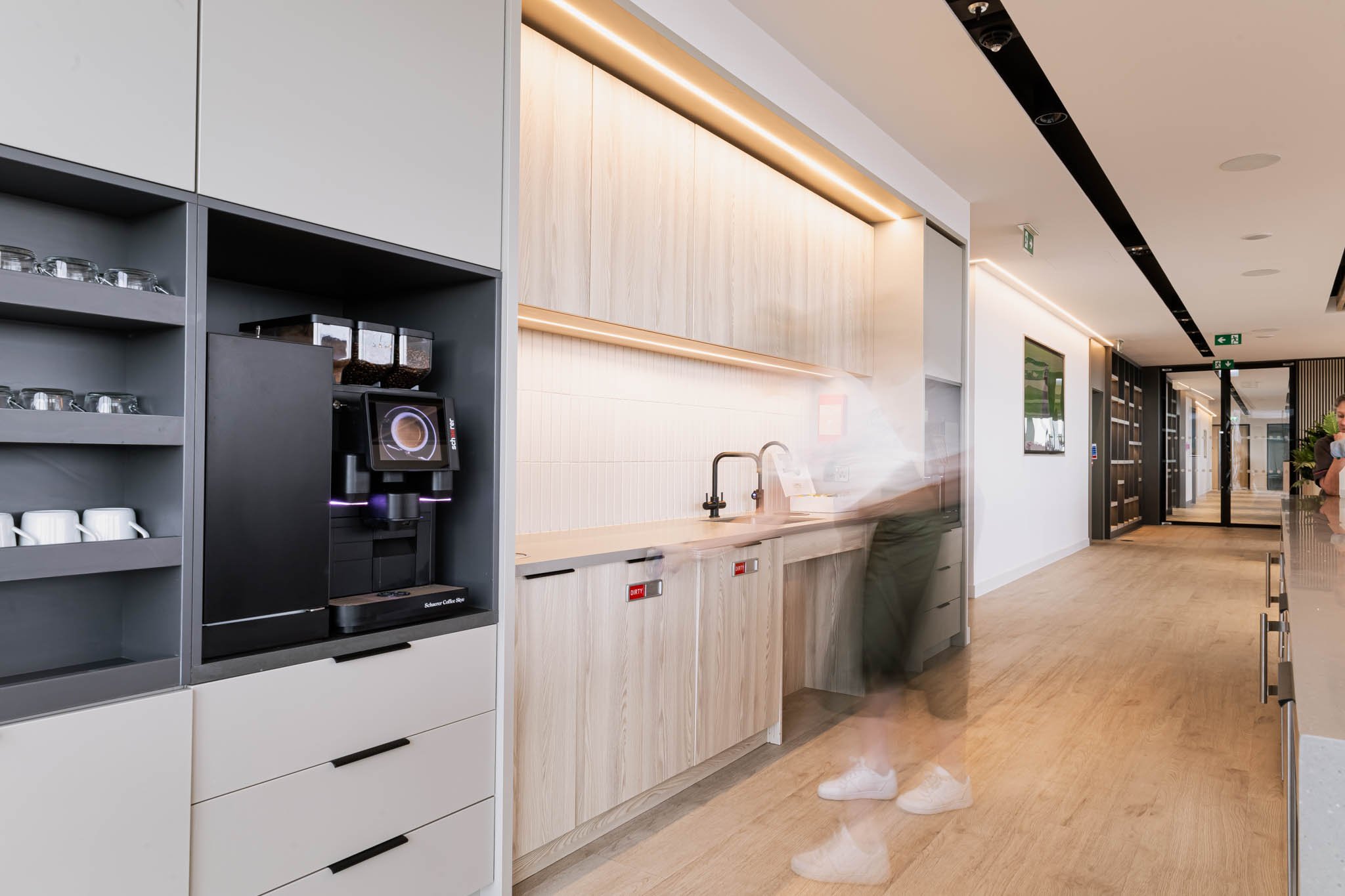 Modern coffee station with a coffee machine, cups, and storage cabinets in a bright, contemporary office kitchen.