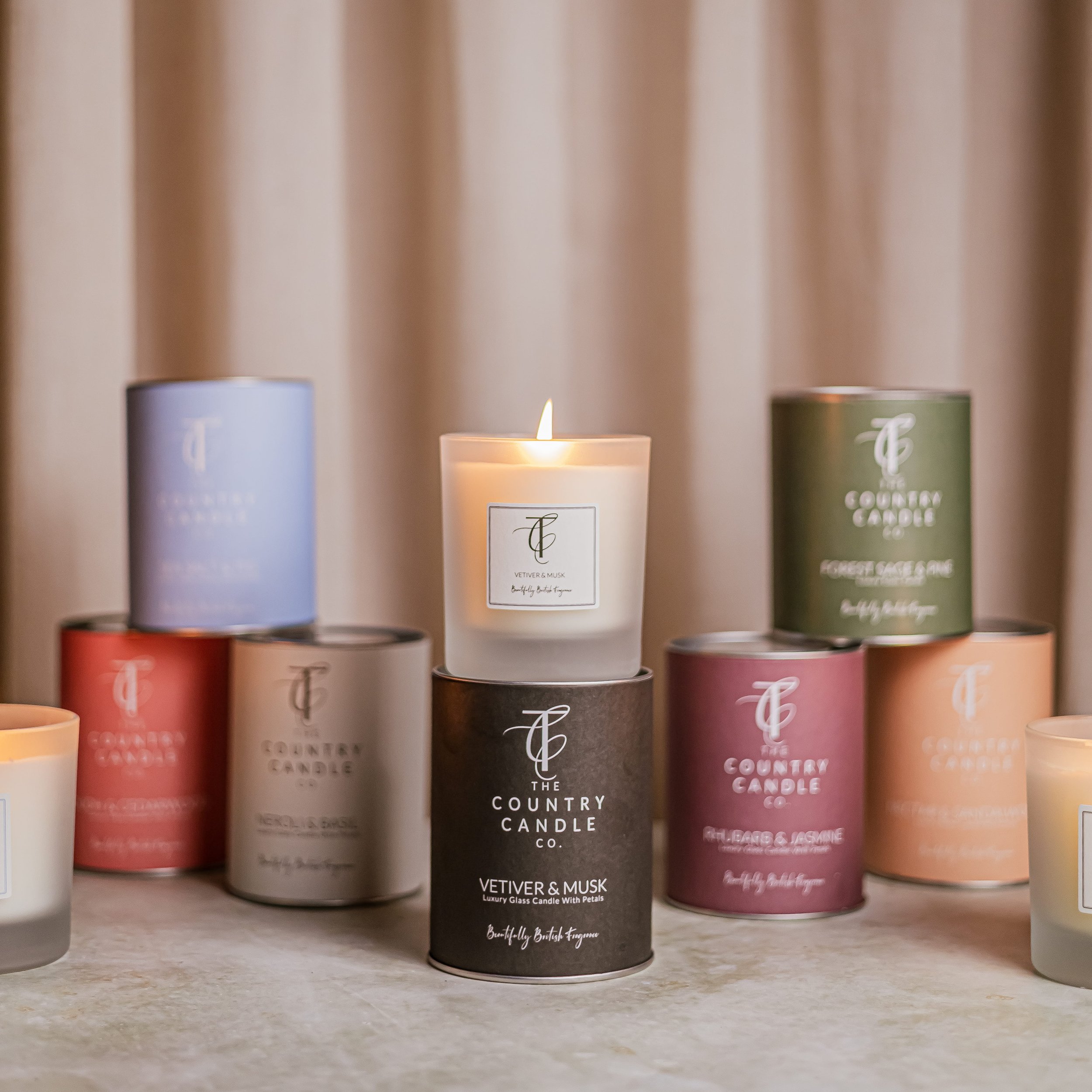 A group of scented candles, with one lit, on a table in front of beige curtains.