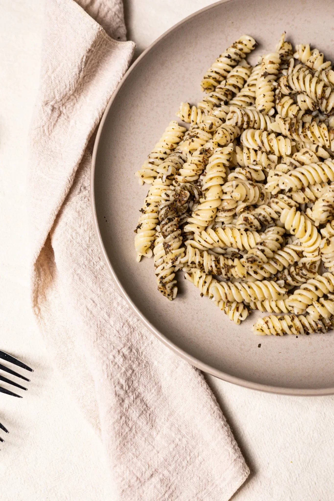 Professional food photography of restaurants Fusilli pasta with herbs on a beige plate, beside a white napkin on a white surface by LensBox Photography