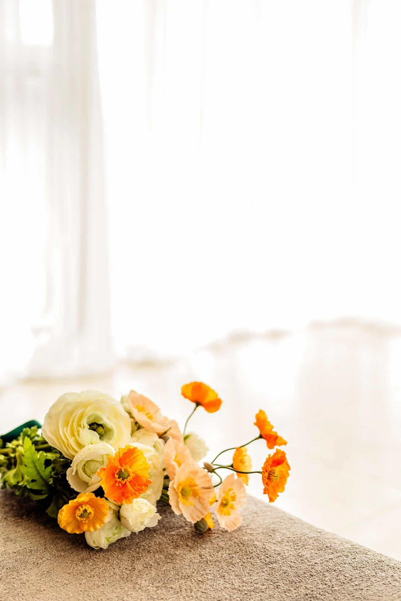 Bouquet of cream and orange flowers resting on a soft surface in front of a bright window.