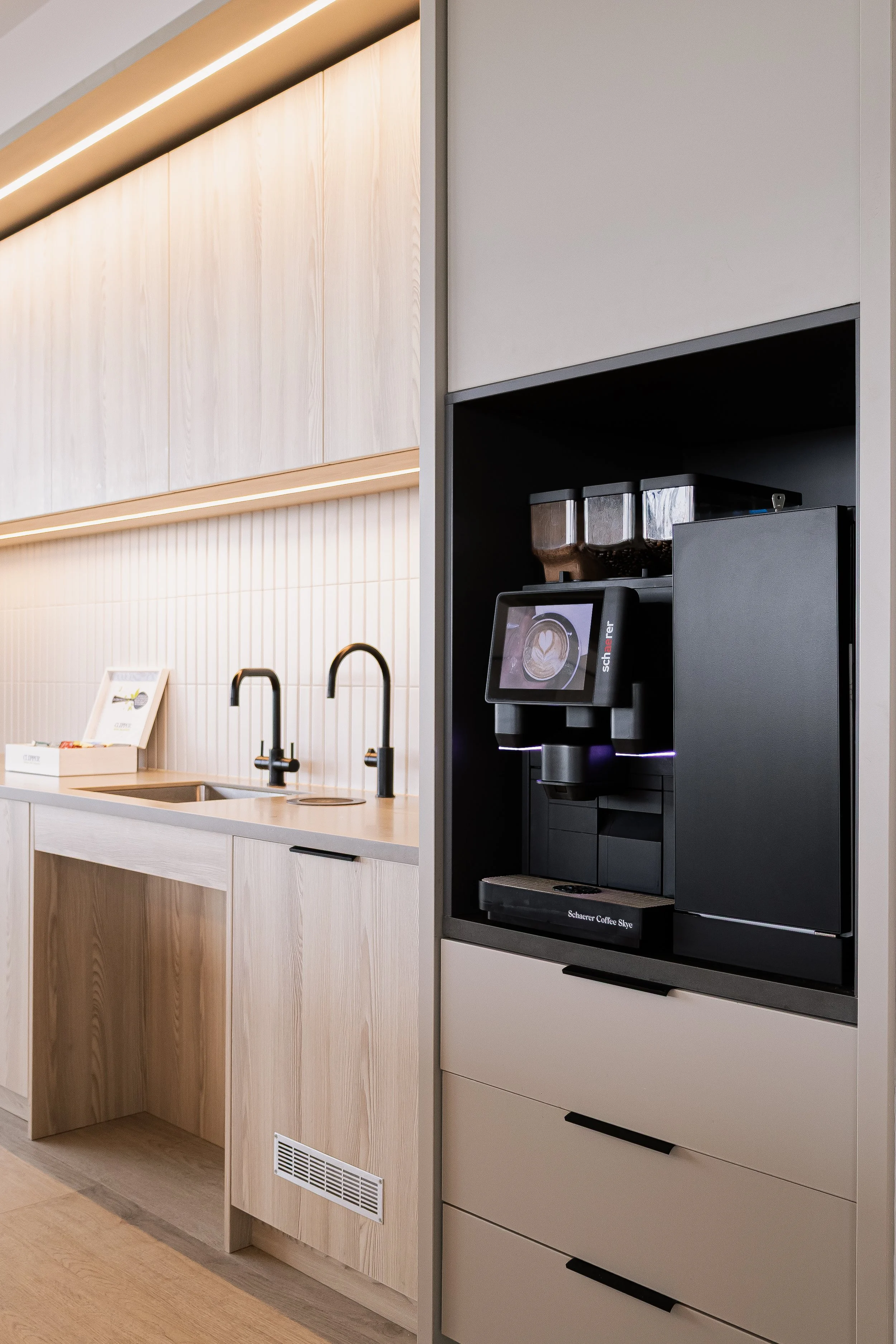 Real estate photography of a Coffee machine in a modern kitchen with light wood cabinets and black faucet in belfast.
