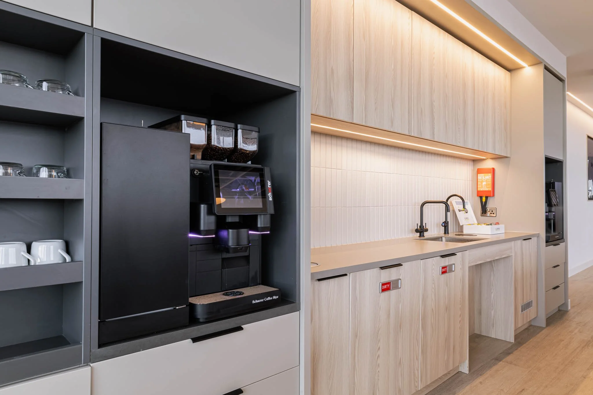 Coffee station with a black coffee machine, glass jars with coffee beans, white cups, and a sink with a faucet in a modern kitchen area.