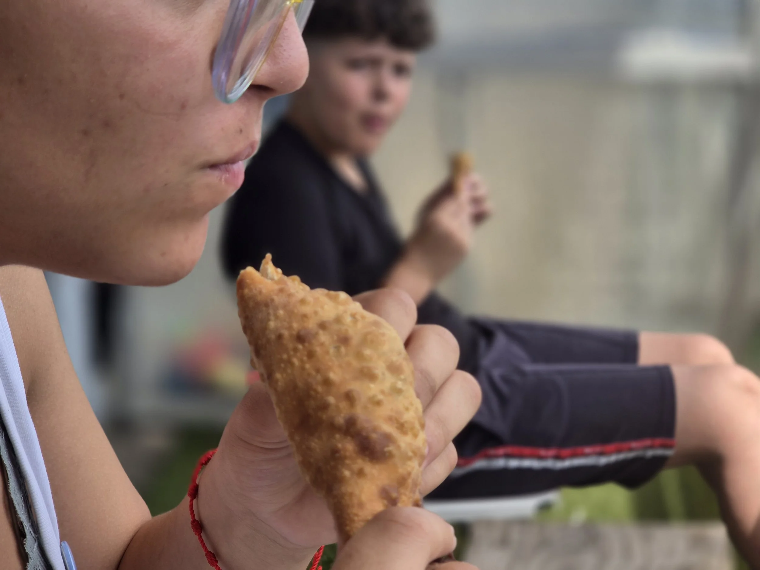Deux enfants mangent des bâtonnets de poisson frits, l'un au premier plan et l'autre en arrière-plan, dans un environnement intérieur.
