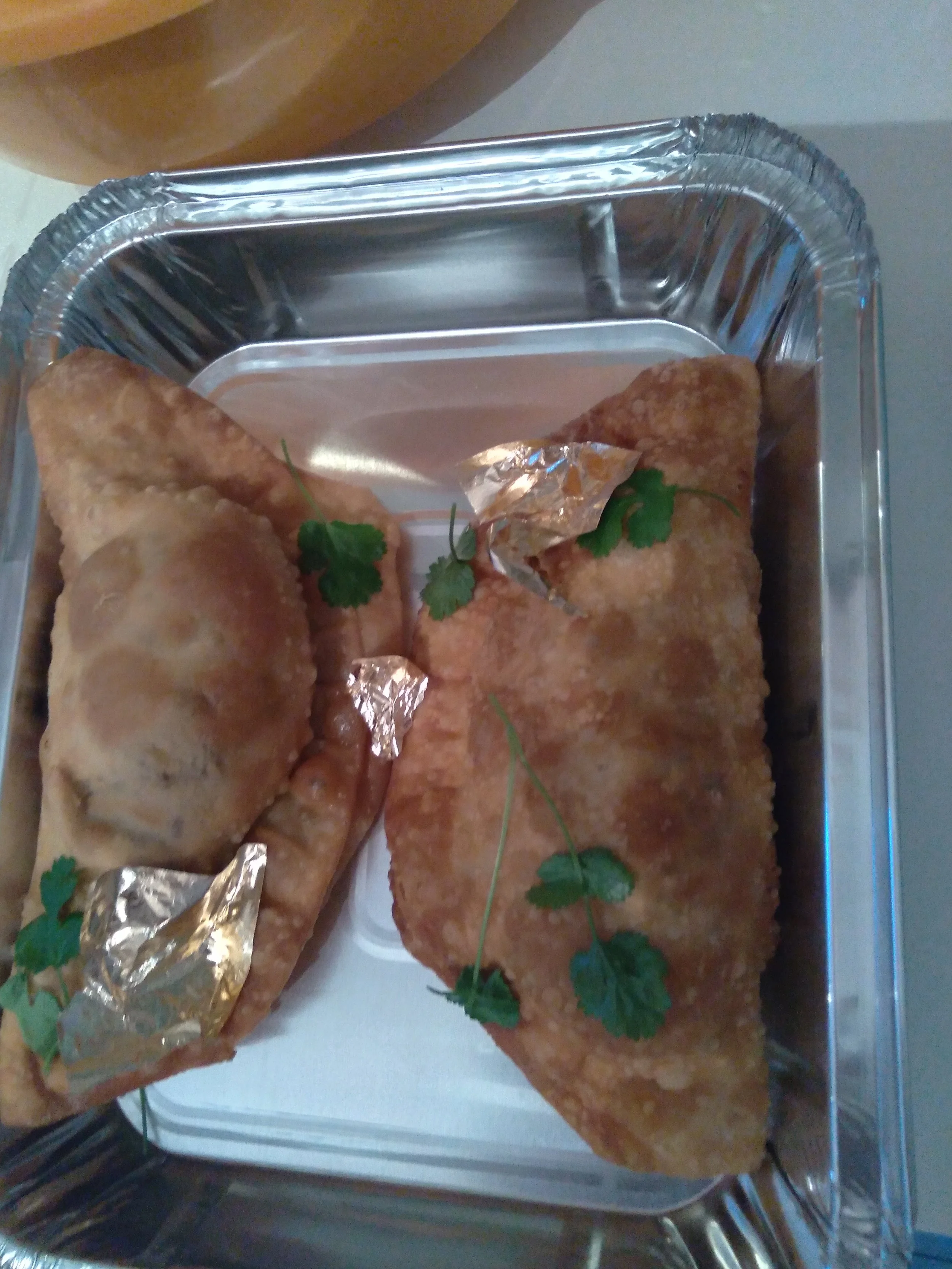 Surtido de empanadas fritas decoradas con ramitas de cilantro, servidas en una bandeja de aluminio.