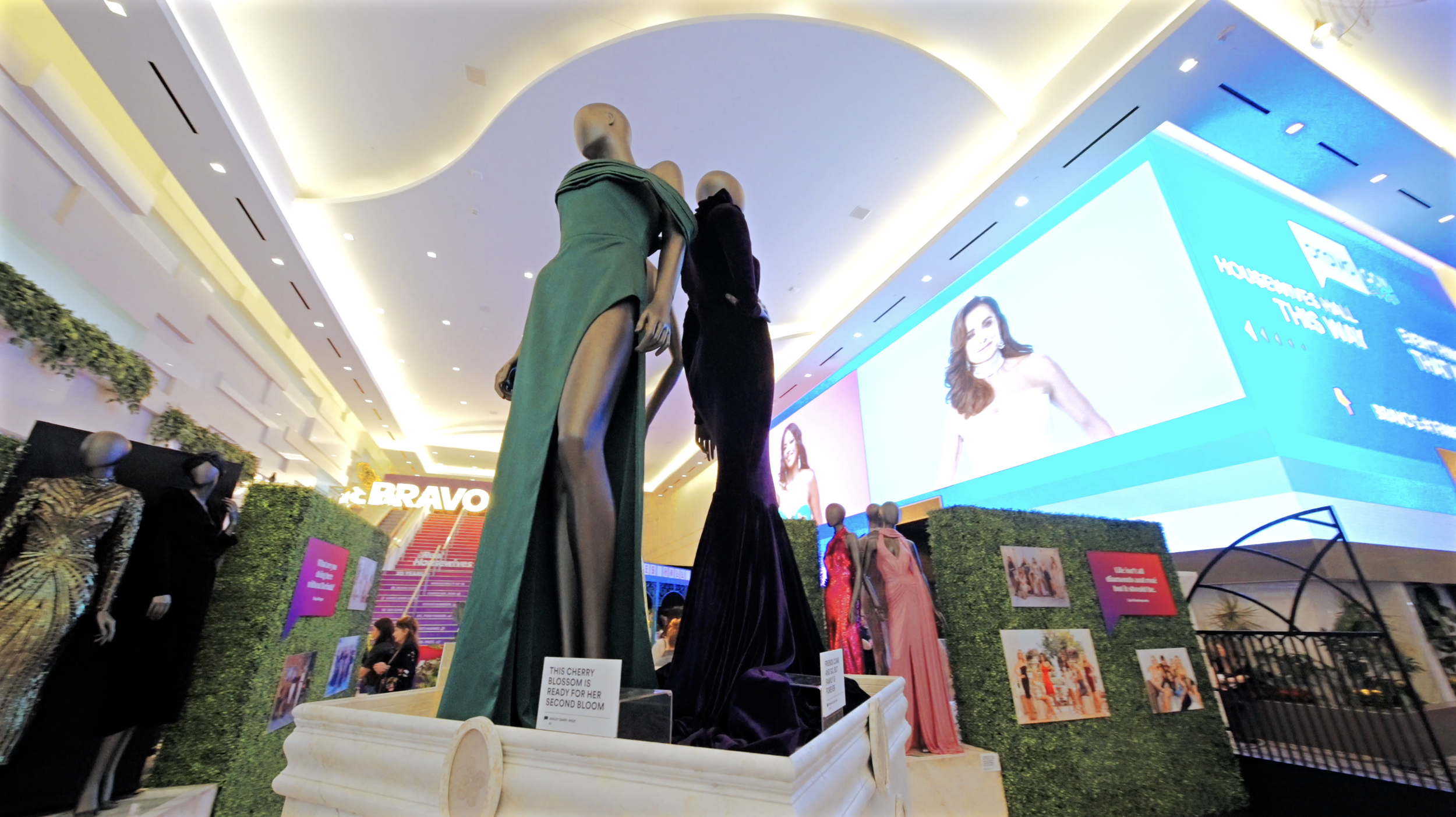 Display of mannequins wearing evening gowns at an indoor fashion event.