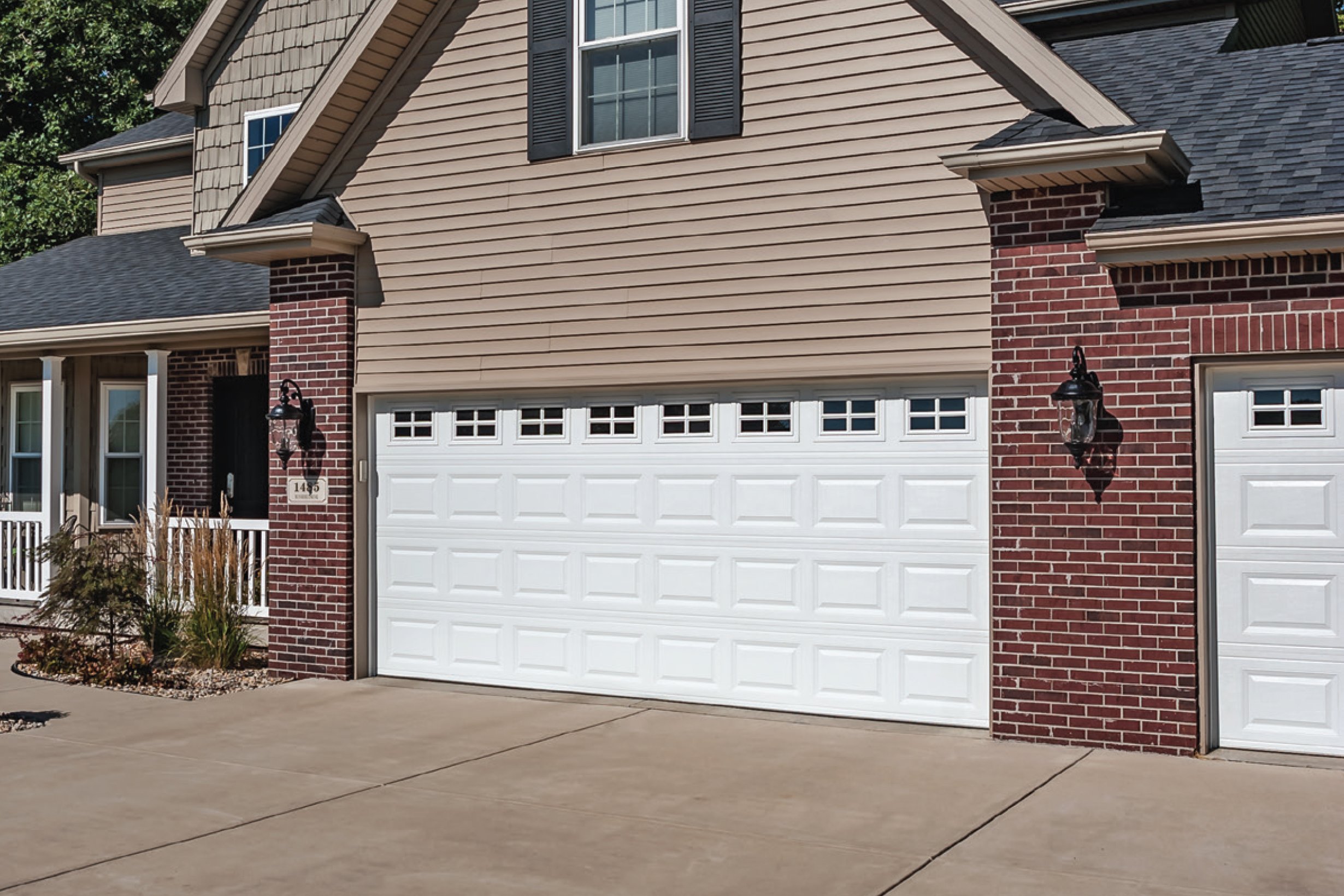 Residential house with brick and beige siding, black shutters, white garage door, and outdoor wall-mounted lanterns.
