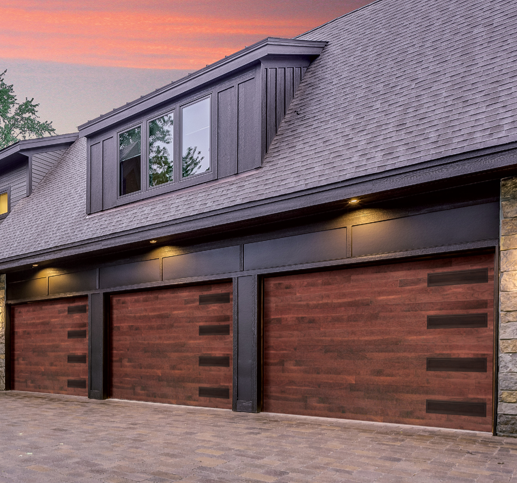 Two garage doors made of wood with black accents on a house with brick and gray siding, under a sunset sky.