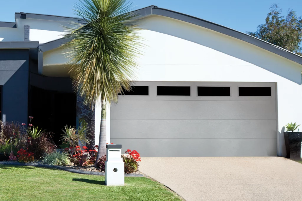 Modern house with a white garage door, a sloped roof, and a small garden with tropical plants and a palm tree in front.