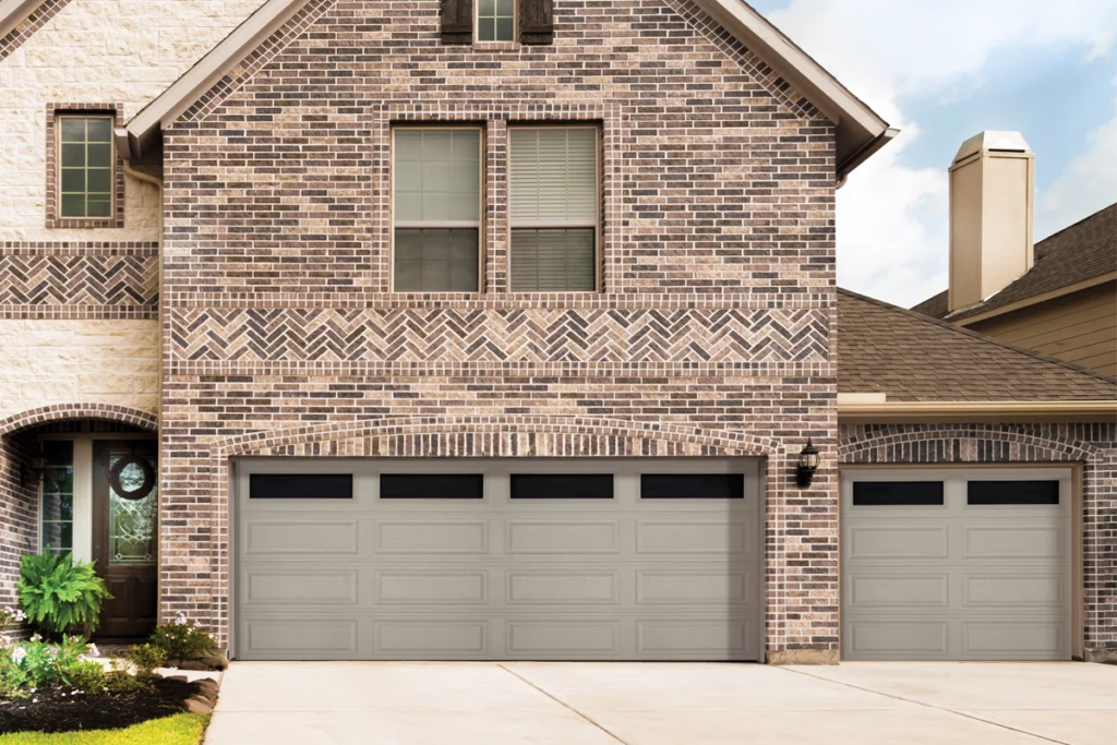 A brick house front with two garage doors and a small garden bed.