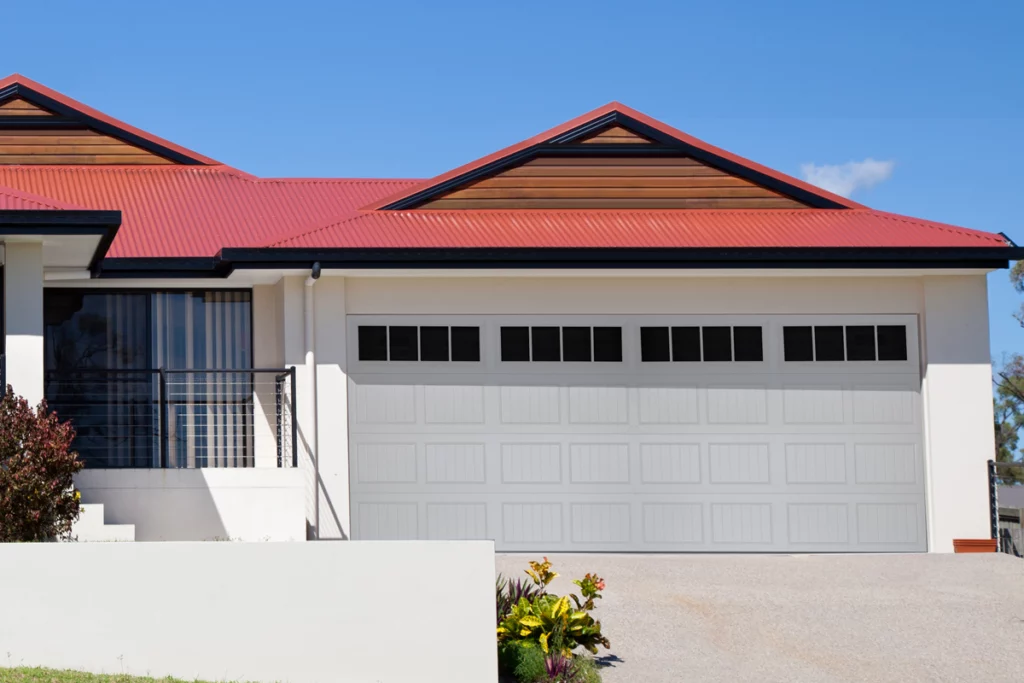Front view of a house with a white garage door, white exterior walls, and a red metal roof under a clear blue sky.
