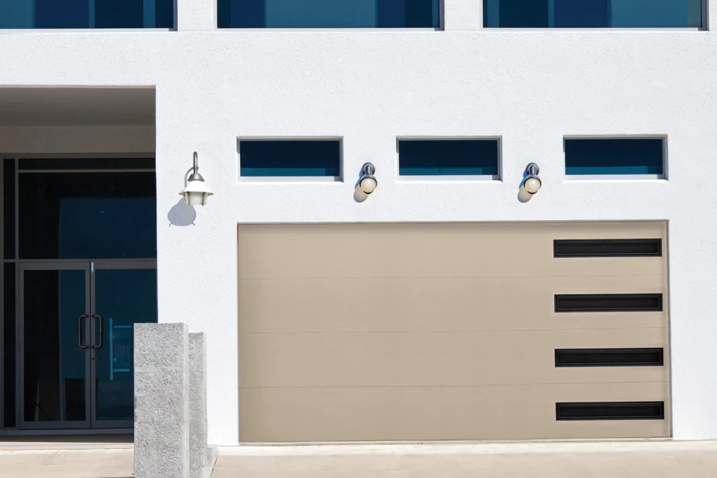 Close-up of modern house entrance with beige garage door, three horizontal small windows, and exterior wall-mounted lights.