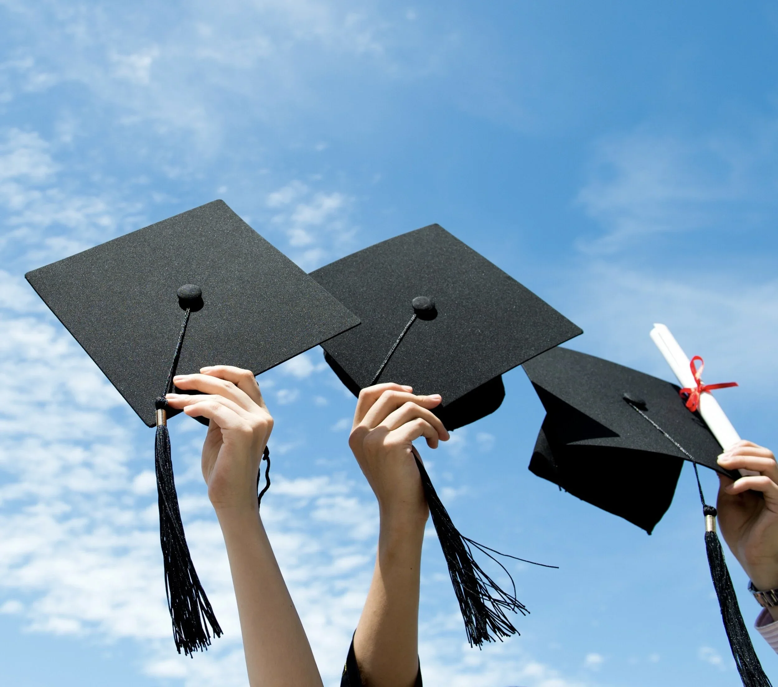 Graduates holding their caps and diploma above their heads against a blue sky.