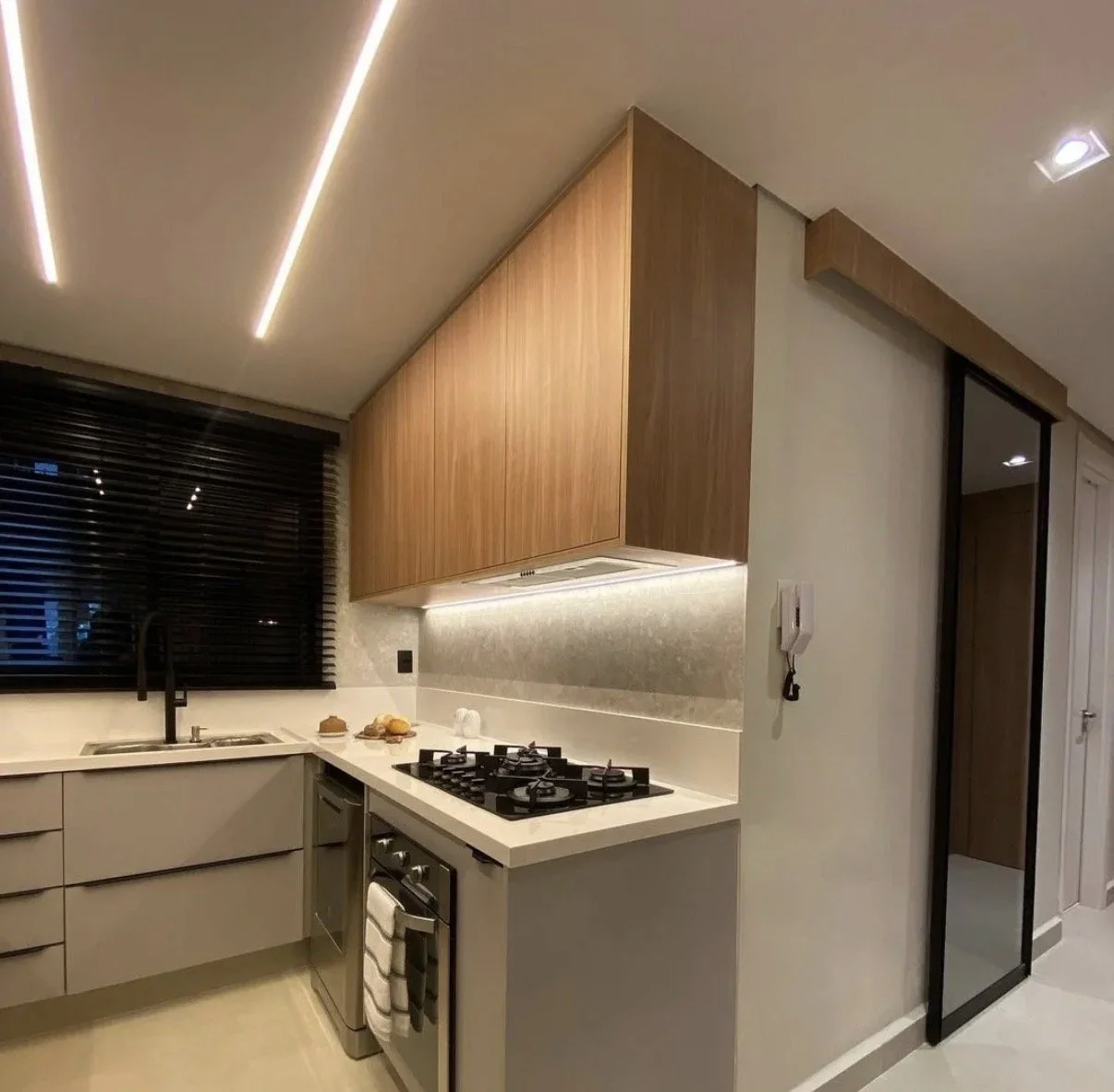 Cocina moderna con armarios de color beige, persianas negras, una cocina de gas con horno, encimera de color beige y una decoración minimalista.