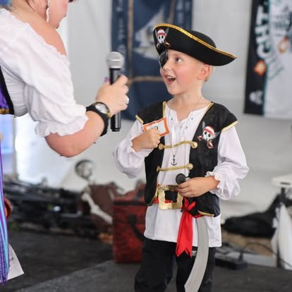 Young boy dressed as a pirate talking to a woman holding a microphone.