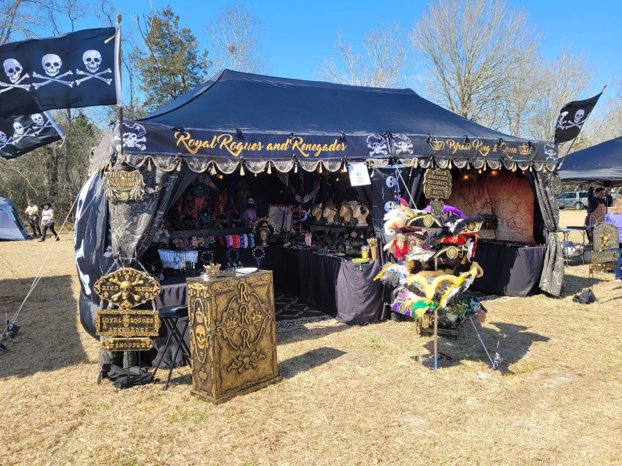 Outdoor vendor booth decorated with pirate-themed accessories and skull imagery, selling jewelry and accessories at a fair.