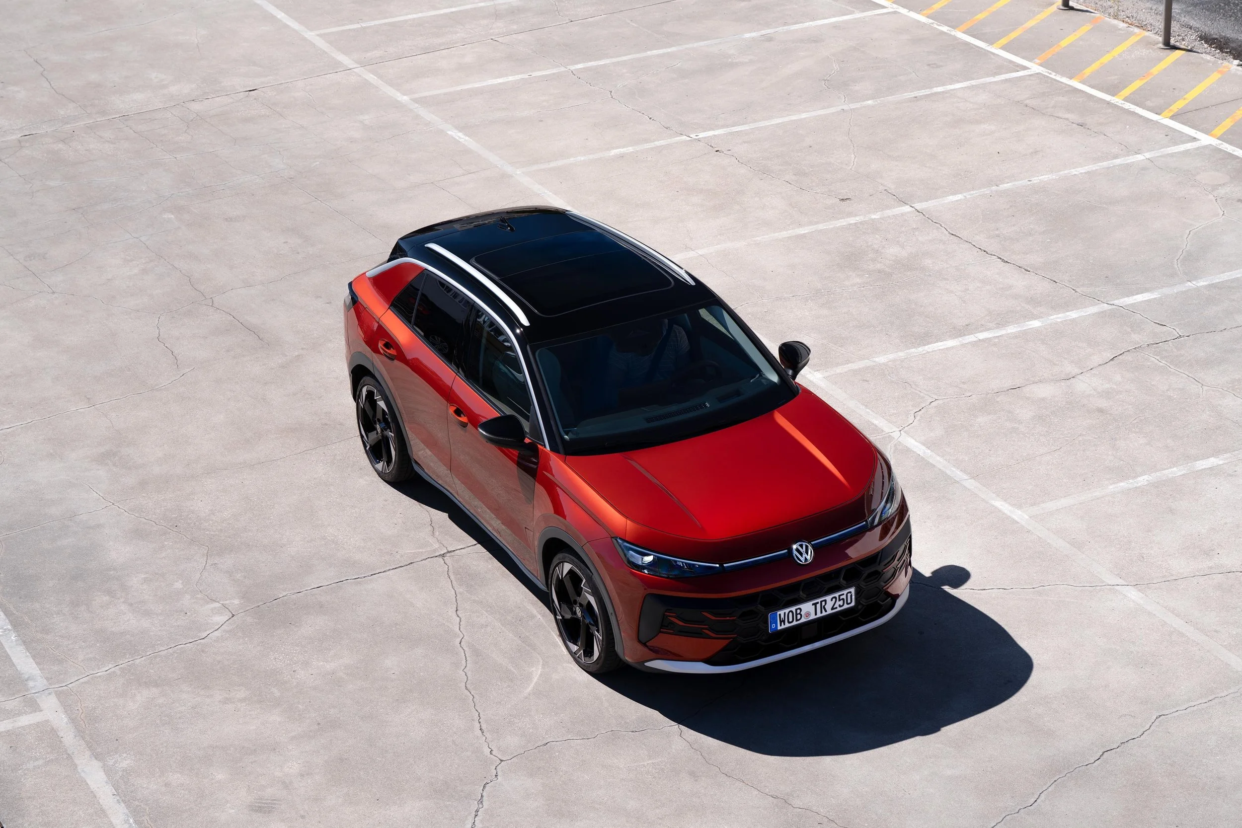A red and black Volkswagen SUV parked alone in an empty parking lot viewed from above.
