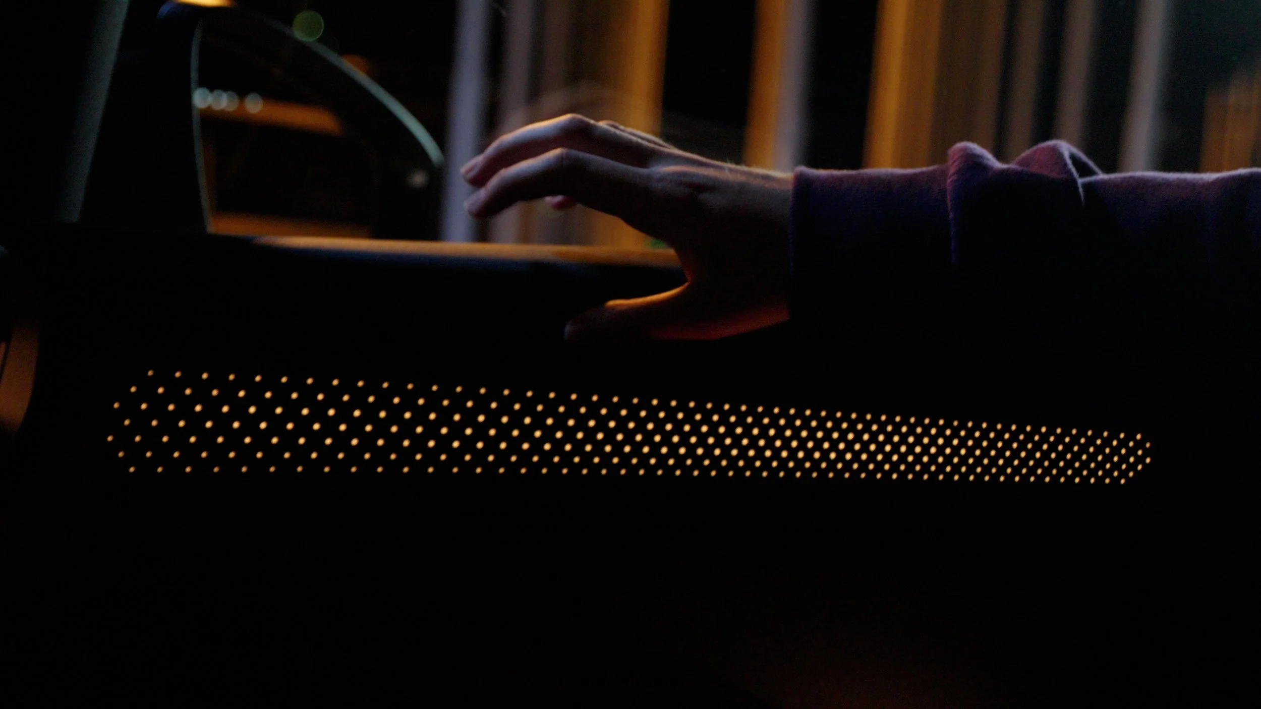 A person touches a device with a perforated yellow front panel, in a dark environment.
