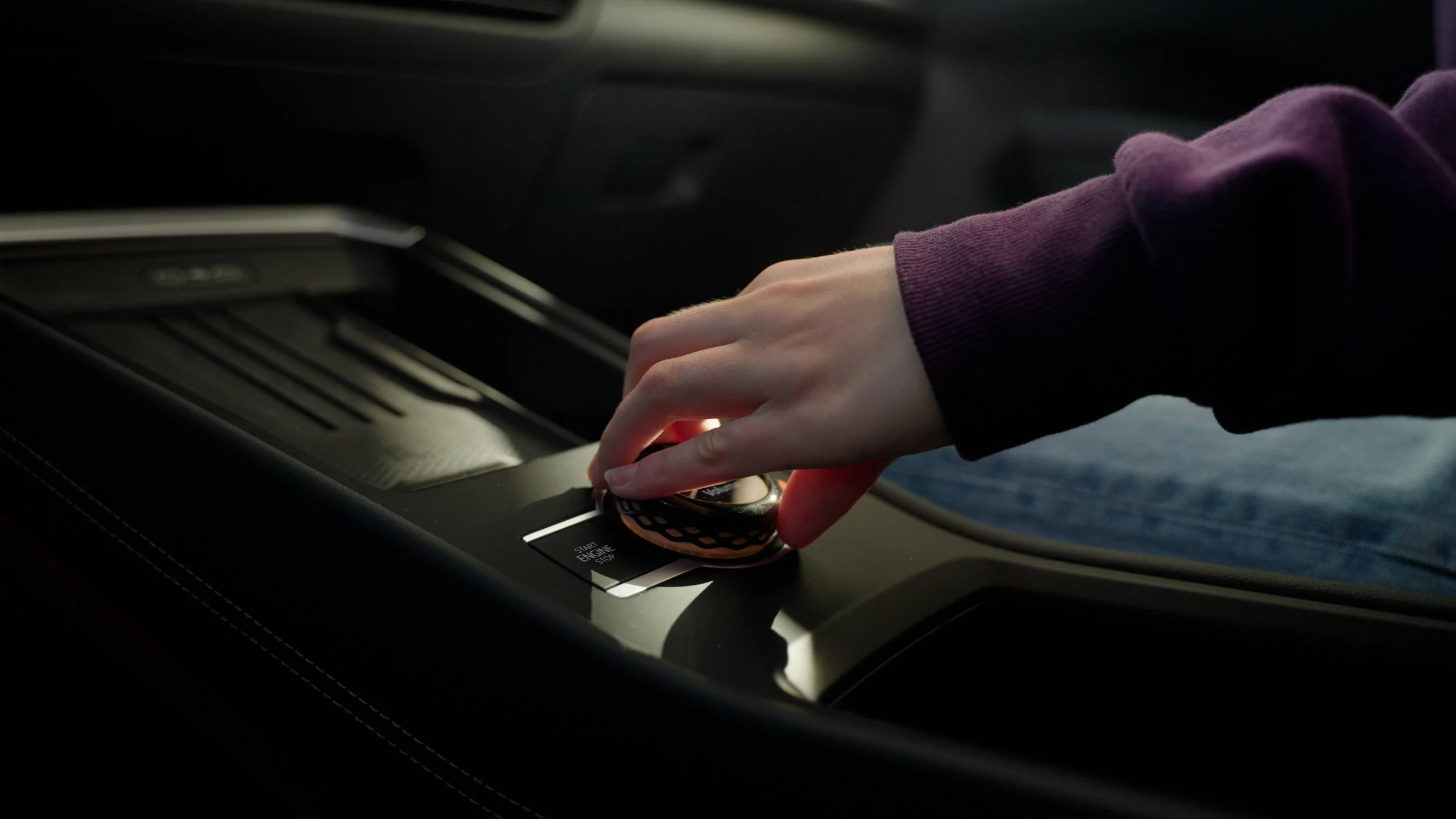 A person pressing the engine start/stop button in a car.