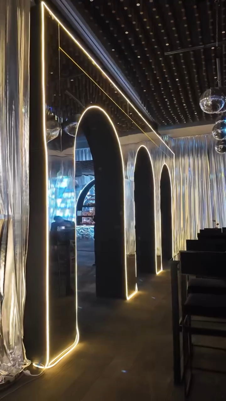 Modern interior with illuminated archways and reflective chrome walls, with decorative hanging glass spheres and a seating area.
