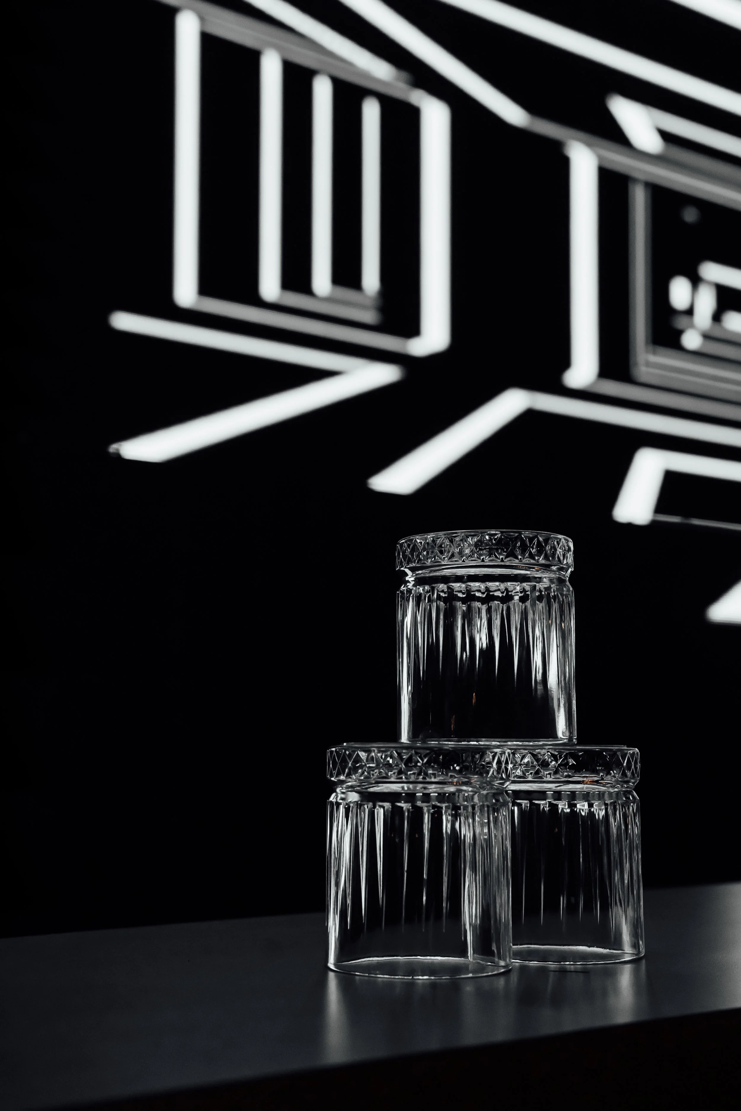 Three clear, patterned glass bowls stacked on a dark surface with illuminated geometric shapes on a black background.
