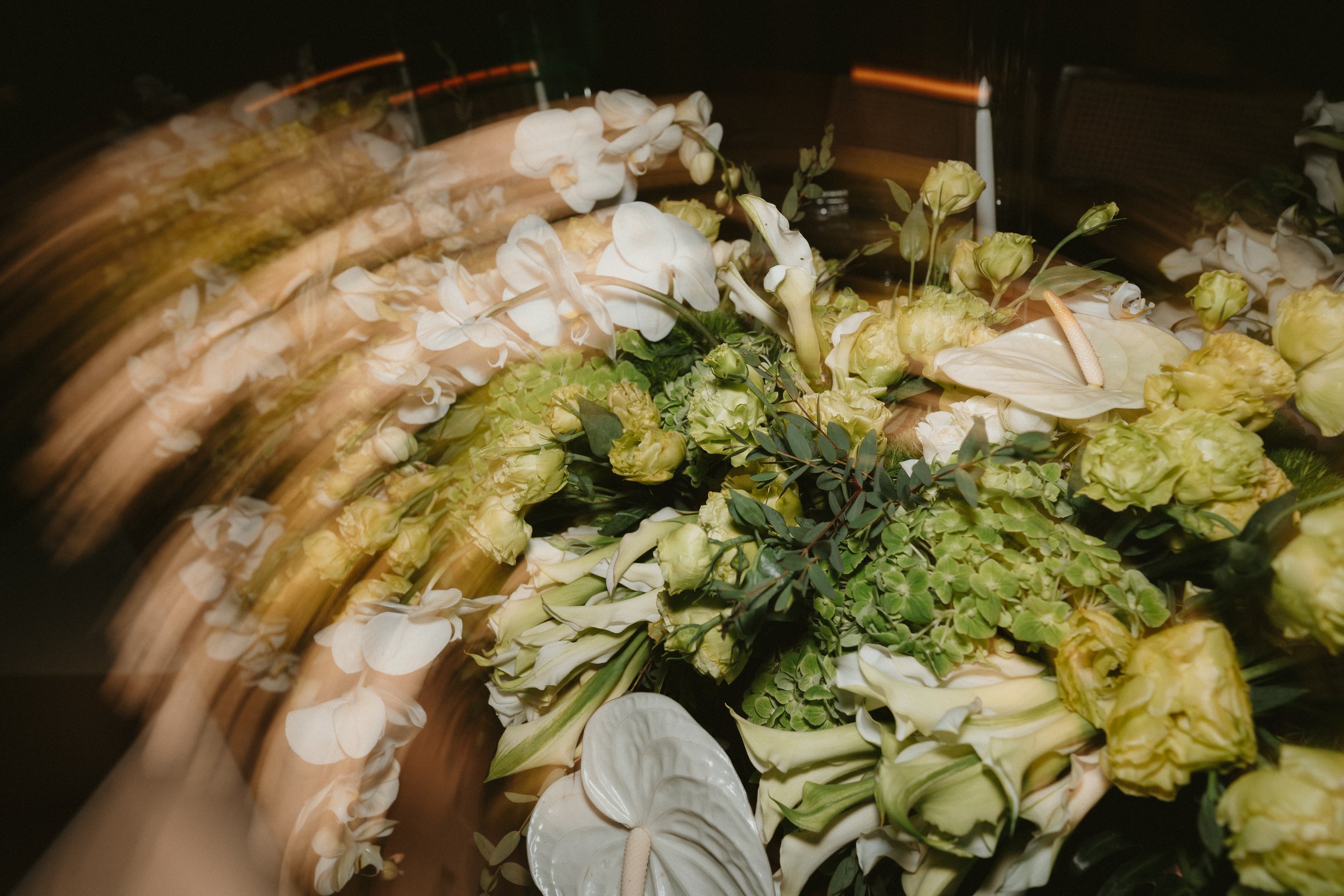 A floral arrangement with white orchids, calla lilies, roses, and greenery, viewed with a motion blur effect.
