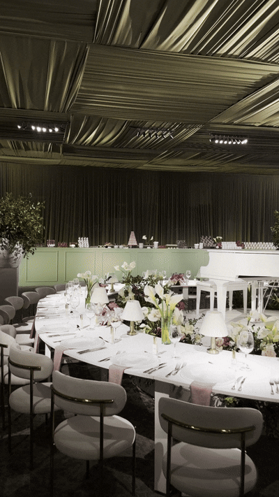 Elegant banquet table decorated with flowers, candles, and tableware in a well-lit event hall with a black ceiling and draped curtains.