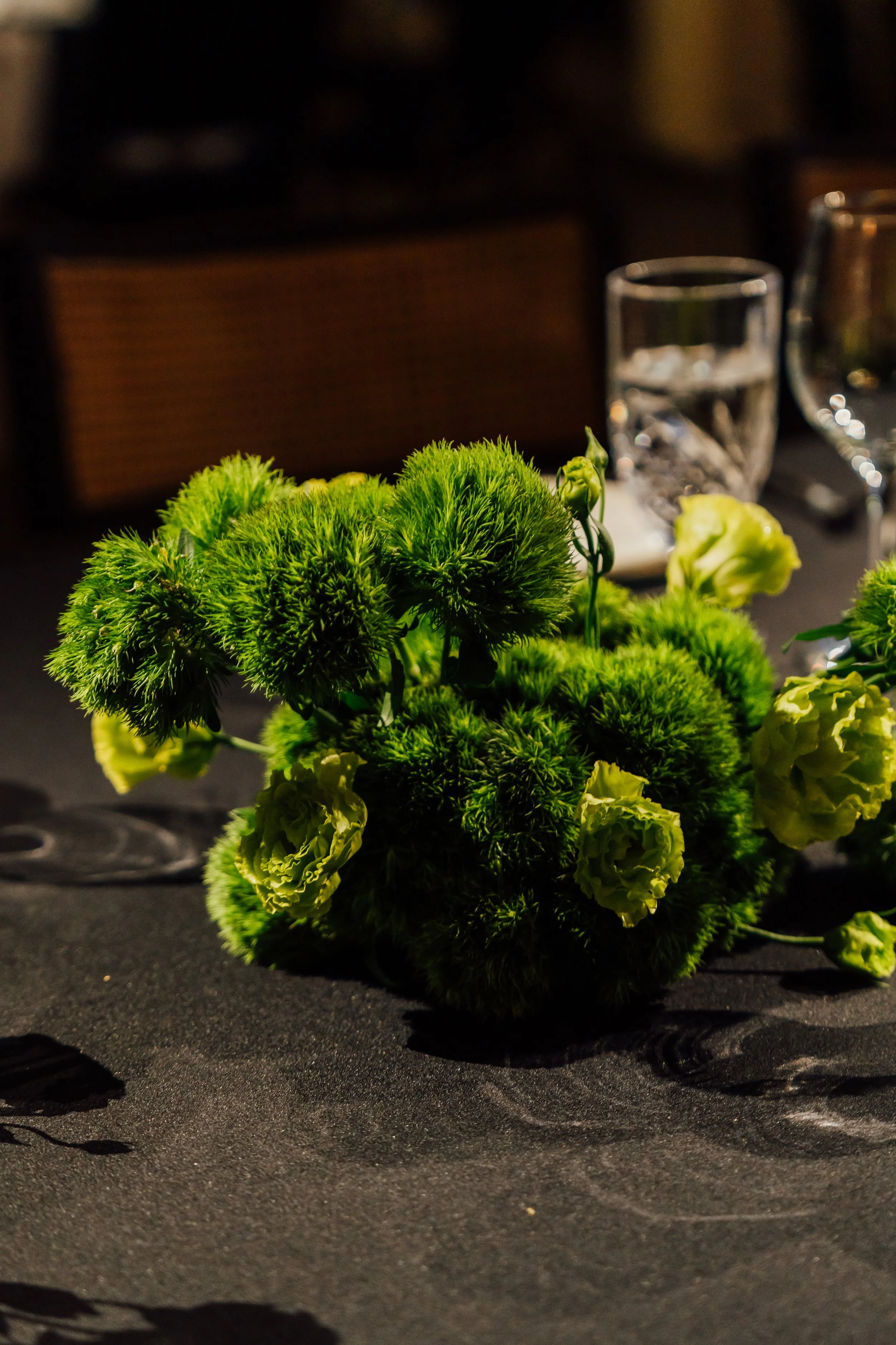 A floral arrangement with green and pale yellow flowers on a black table at a formal event.