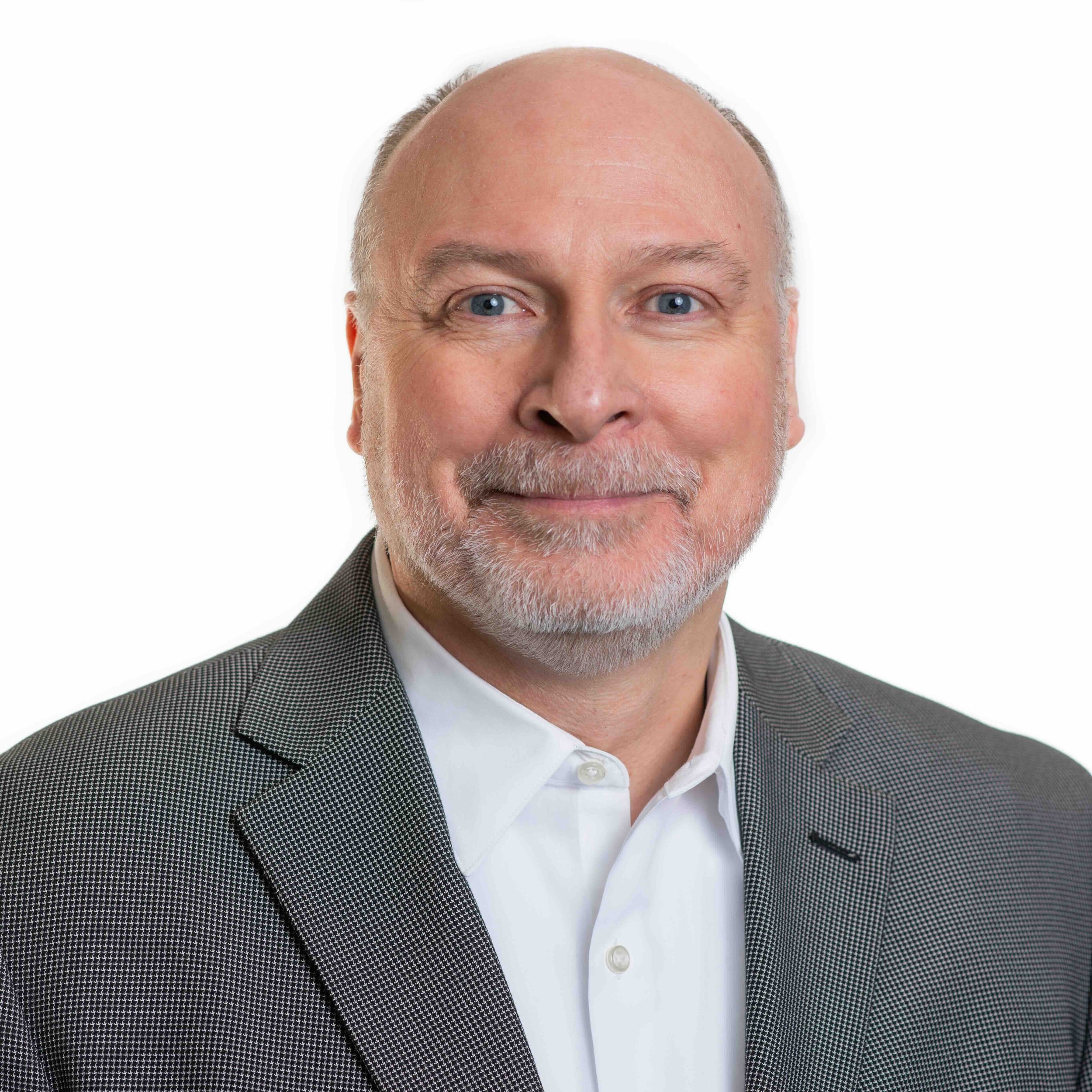 Close-up of Bill Boss with a white beard, wearing a suit and a white shirt, smiling gently against a plain white background.