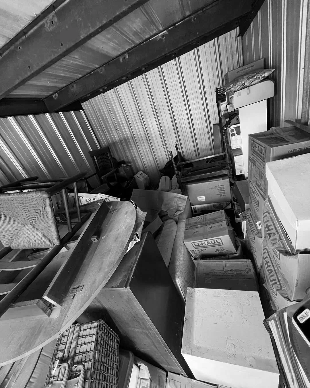 A cluttered storage space with stacked cardboard boxes, furniture, and miscellaneous items.