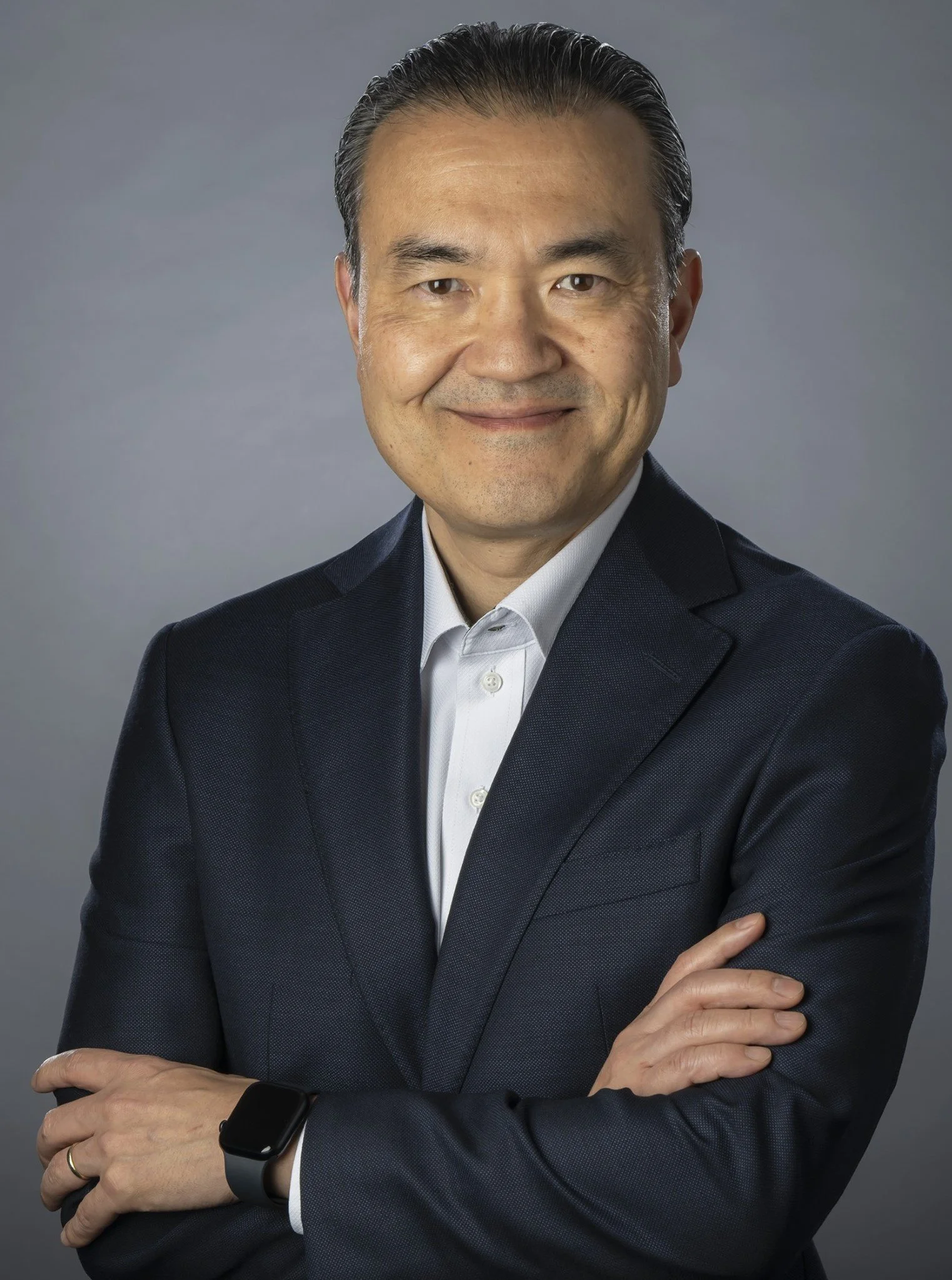Prof. Kazuhiro Yasufuku- A professional man in a suit with a smartwatch on his wrist, standing with his arms crossed, smiling at the camera.