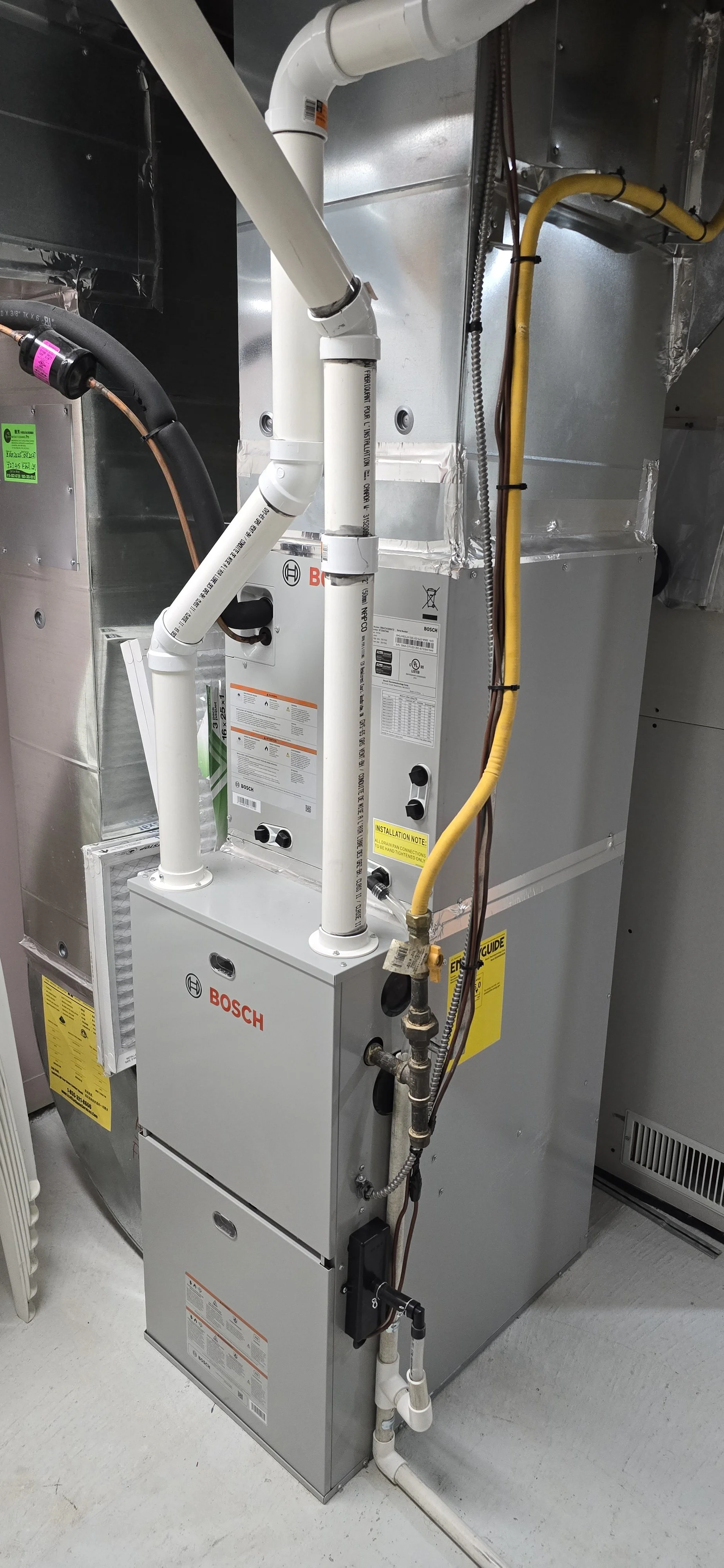 A close-up view of a Bosch furnace or HVAC unit installed inside a utility room with pipes, wires, and vents visible.