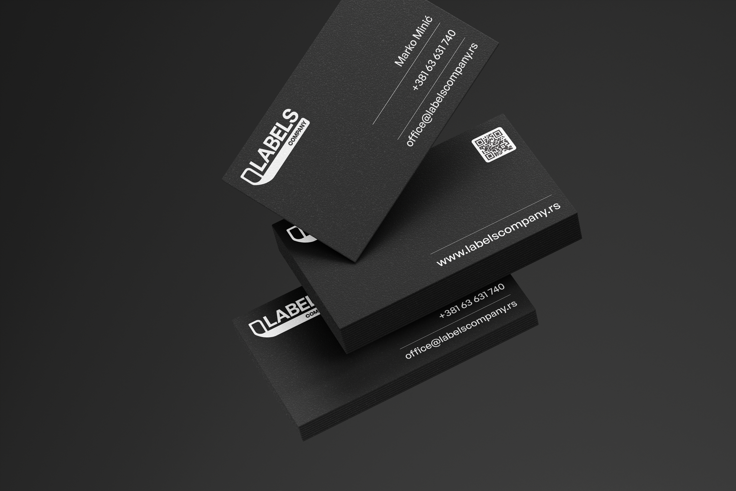Stack of black business cards with white text, showing contact information and a QR code on a dark surface.