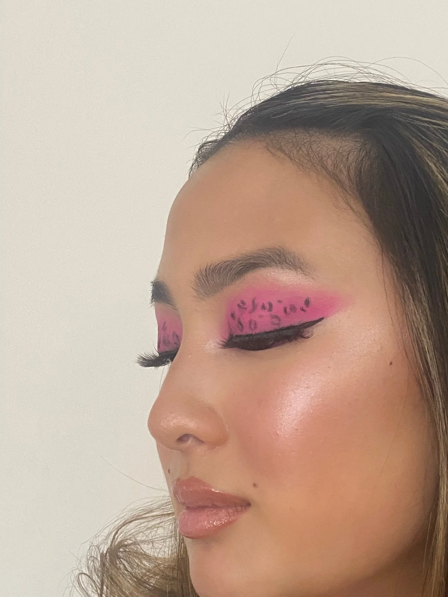 Close-up of a woman with pink and black animal print eye makeup, winged eyeliner, and natural-looking lips.