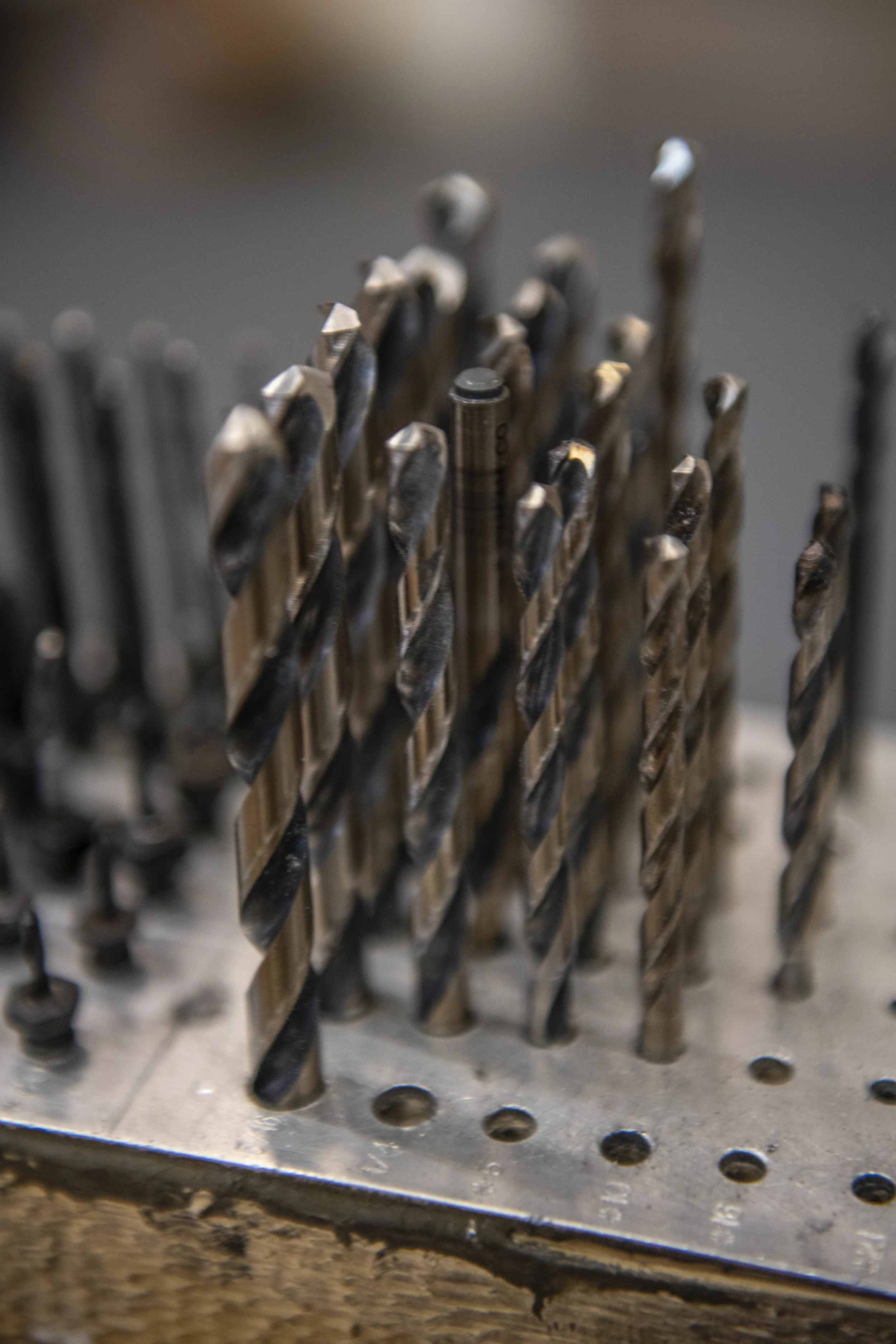 Close-up view of a metal drill bit holder with various drill bits arranged vertically, showing the sharp, twisted edges of the drill bits.