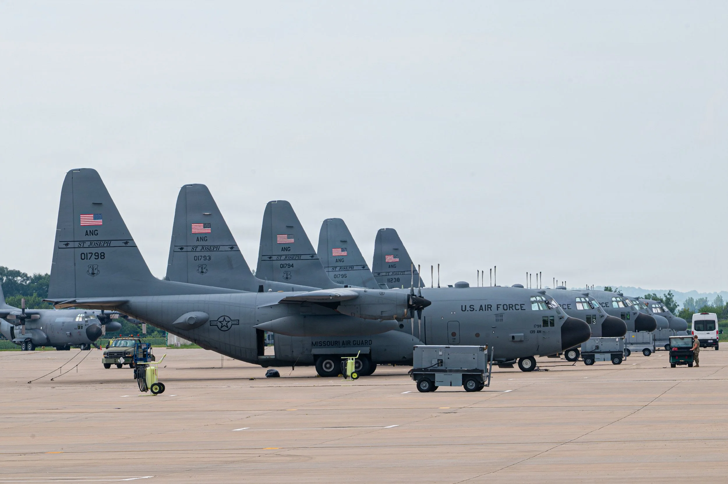 Multiple U.S. Air Force aircraft, including KC-135 Stratotankers and cargo planes, parked on a tarmac with equipment and personnel nearby, under a cloudy sky.