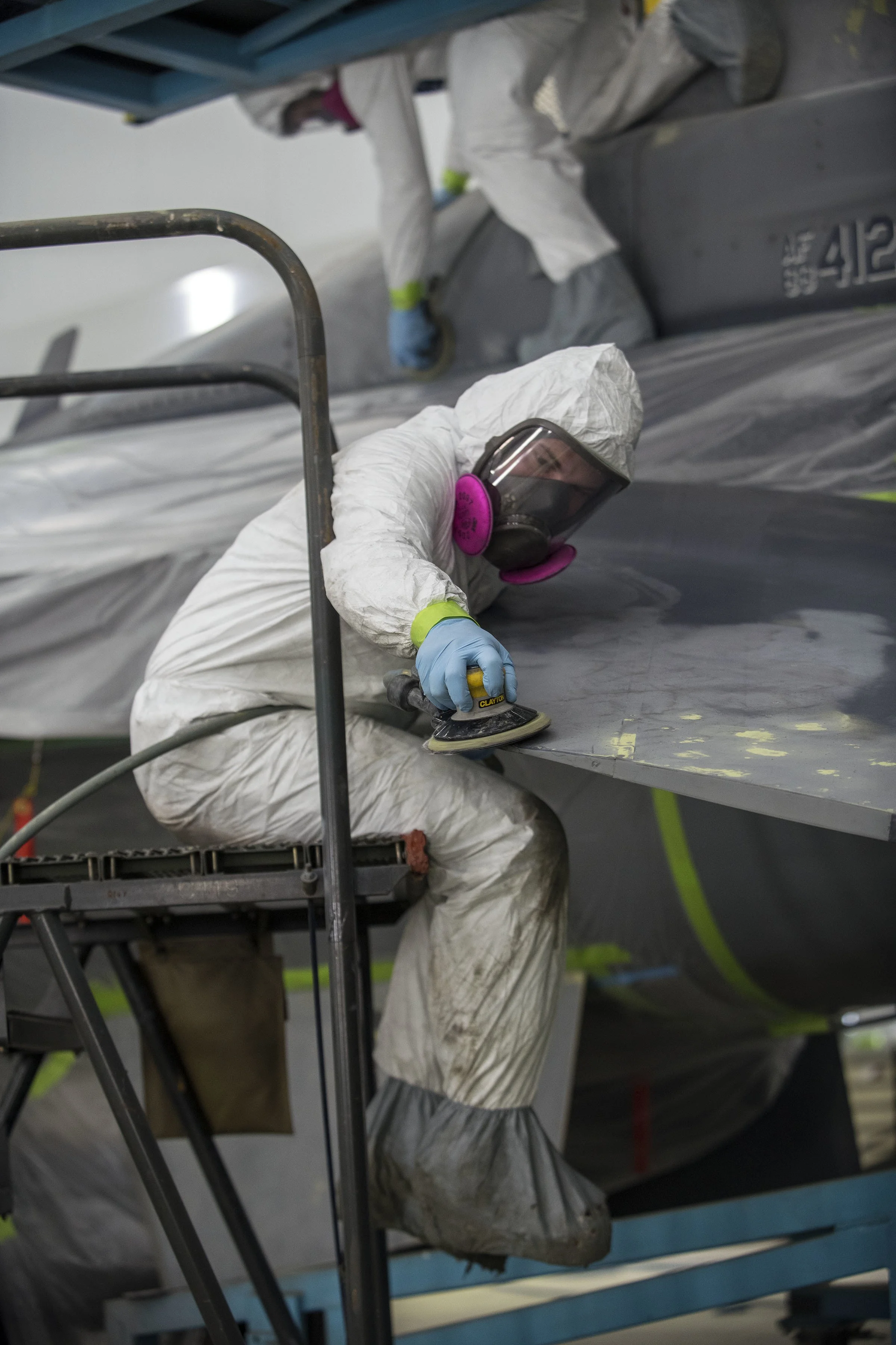 Person in protective suit working with polishing tool on a surface in an industrial setting.