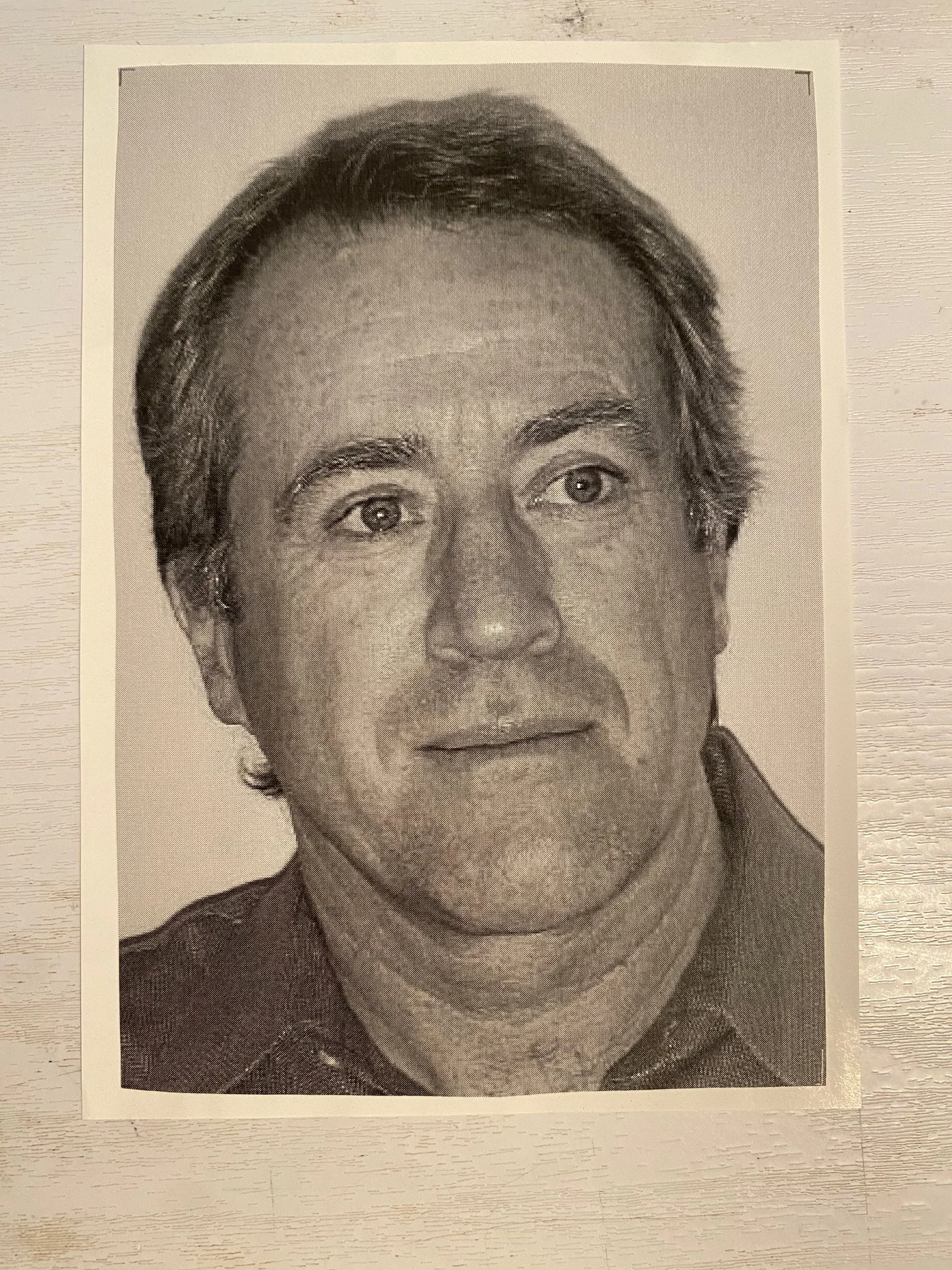 Black and white passport-style photograph of a man with short, dark hair and light skin, wearing a collared shirt and jacket, looking directly at the camera with a neutral expression.